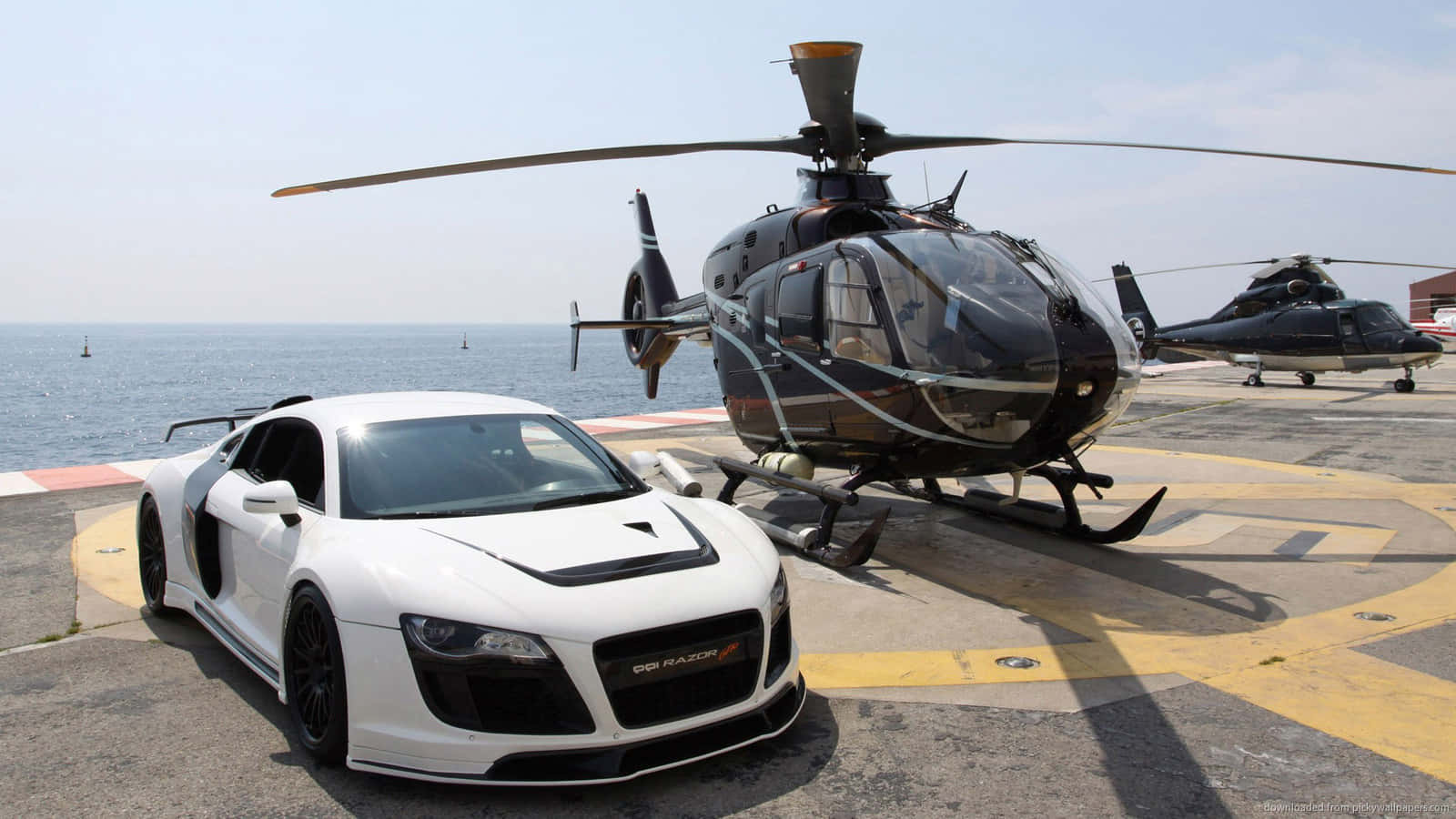 白色跑車和黑色直升機在海邊直升機停機坪上。