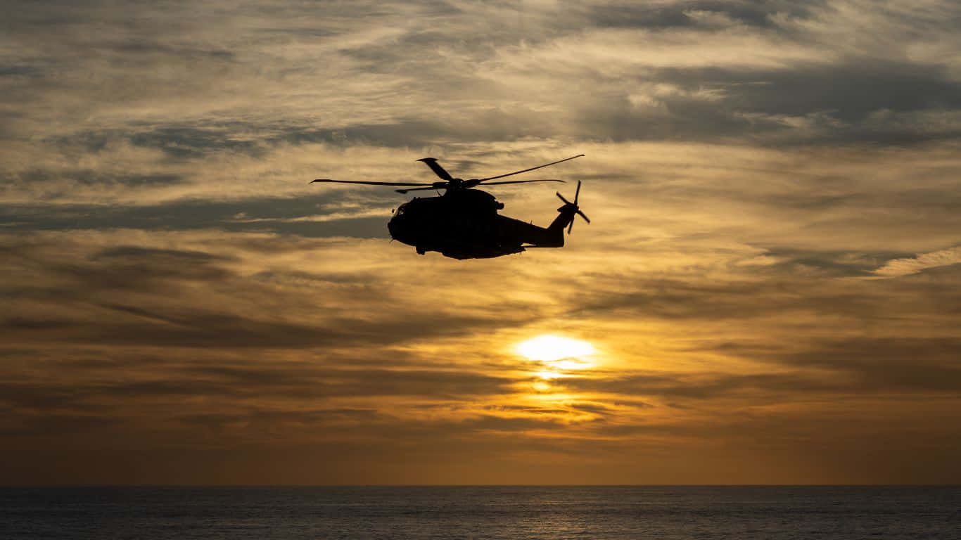 直升機高飛雲層之上 壁紙 — 直升機的剪影在平靜的海面上，襯著金黃色的日落天空翱翔。