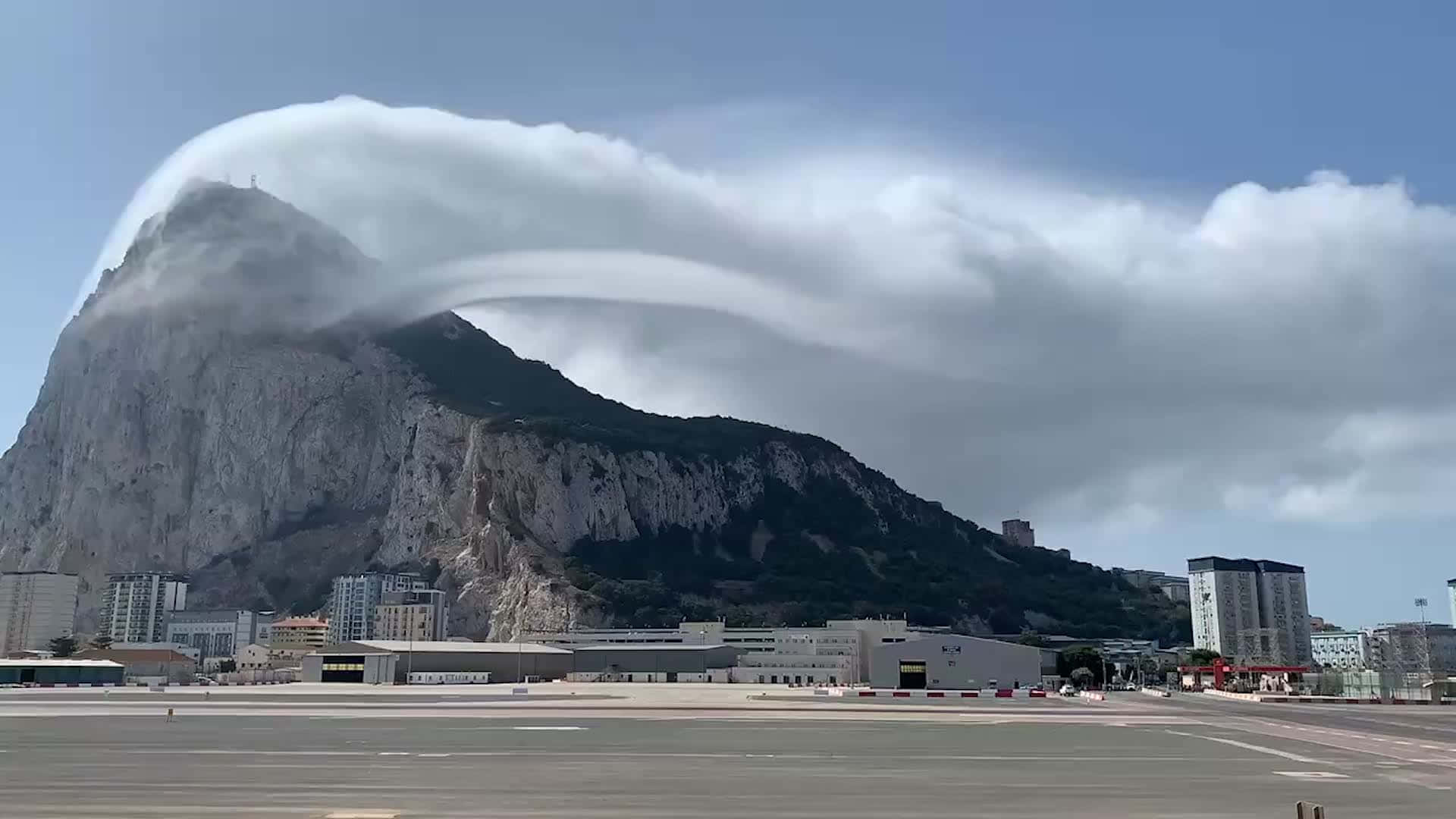 直布羅陀岩雲霧流動 壁紙 — 一團戲劇性的透鏡狀雲完美地懸浮在直布羅陀岩的鋸齒狀山峰上方，下方是城市建築。