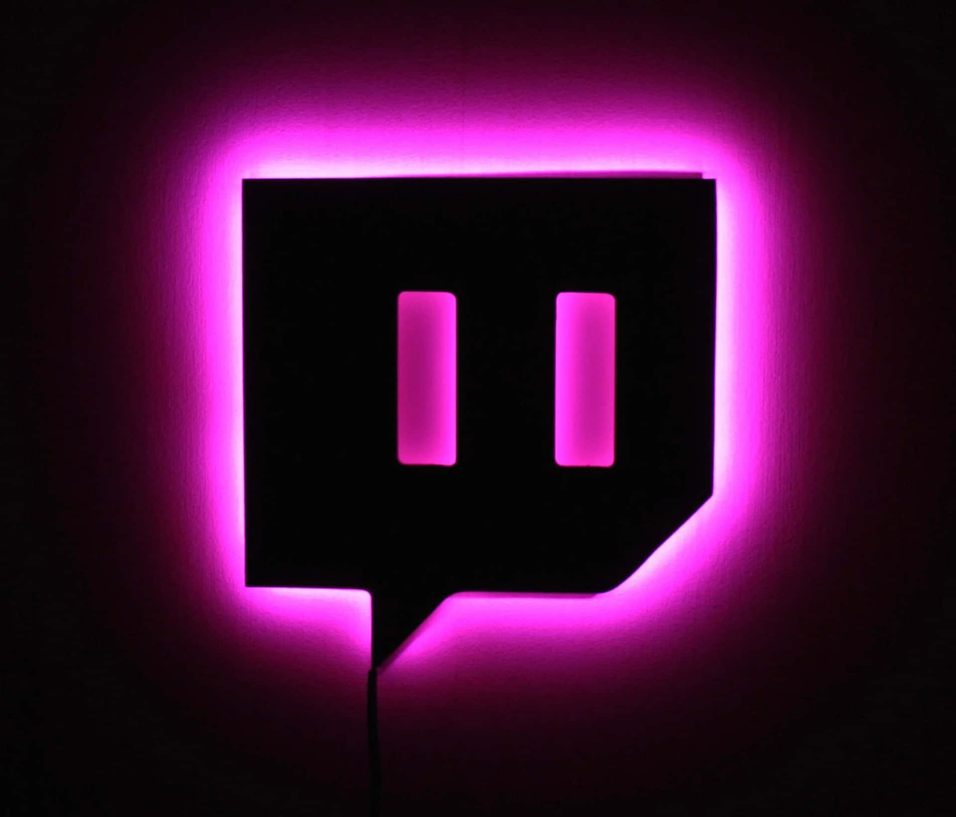 一個發光的粉紅色Twitch標誌安裝在深色牆上。