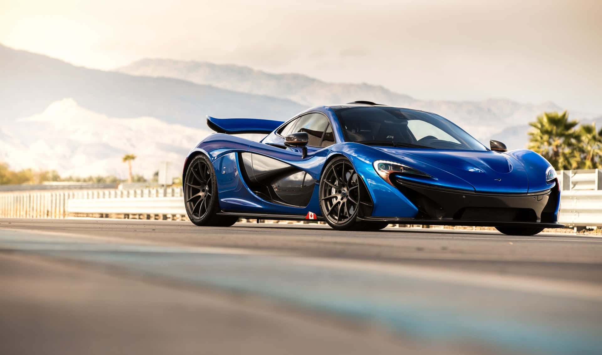 藍色McLaren P1超級跑車在沙漠公路上，背景有山脈和棕櫚樹，夕陽西下。