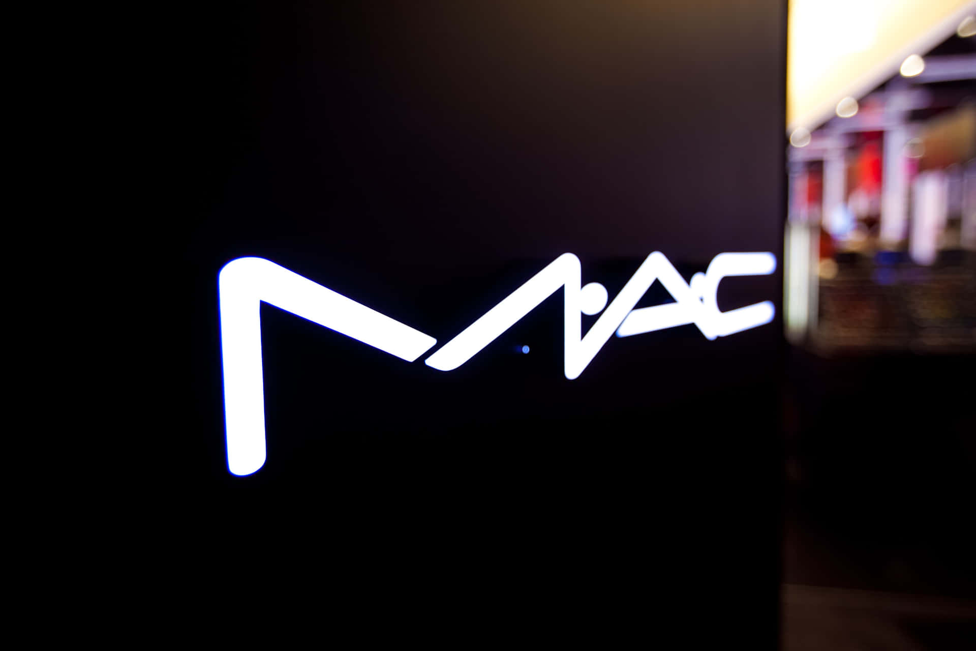 黑暗零售空間中的發光白色MAC標誌招牌。