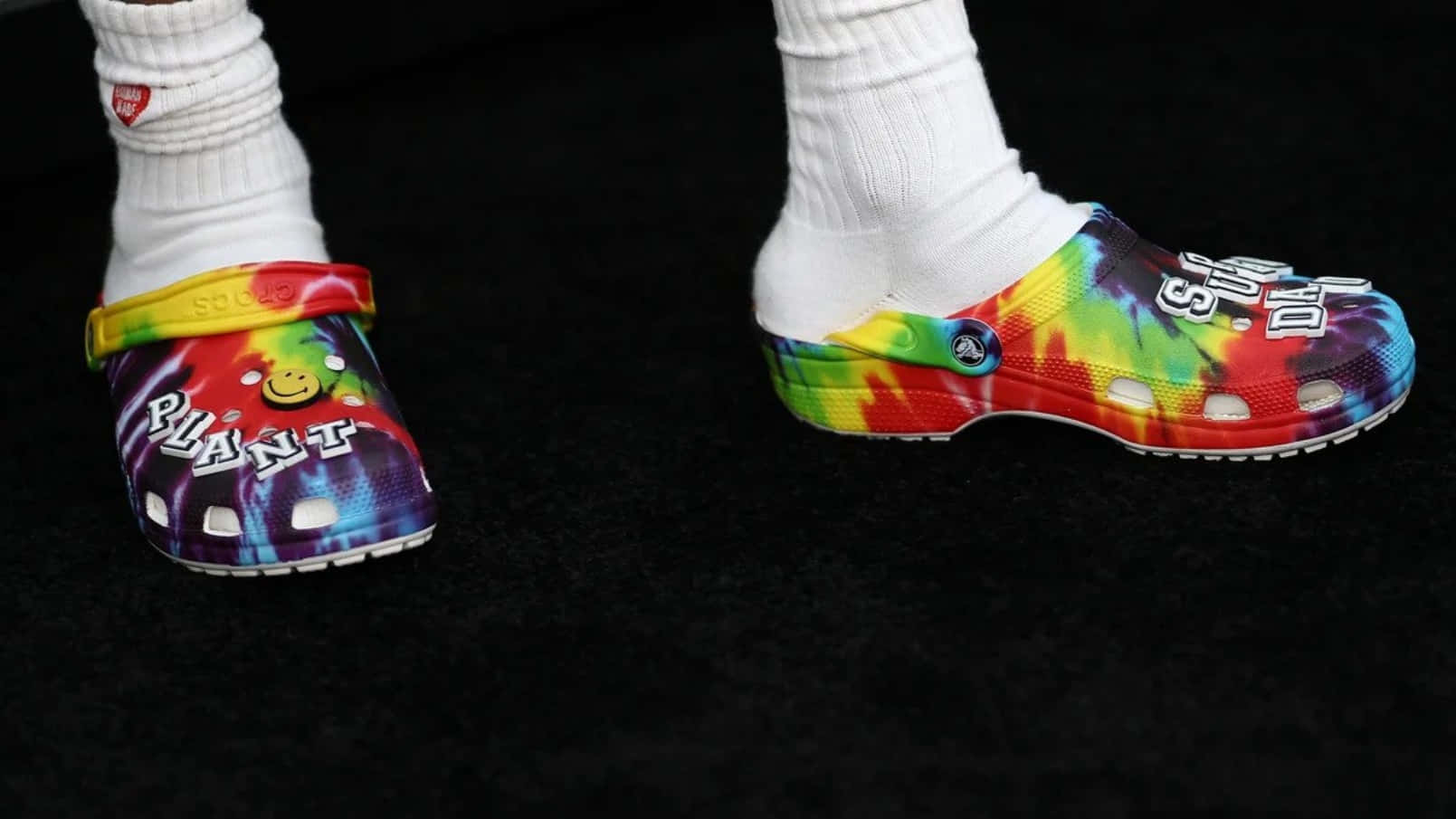 黑色地毯上穿著白色襪子的彩色紮染Crocs，帶有圖形文字。