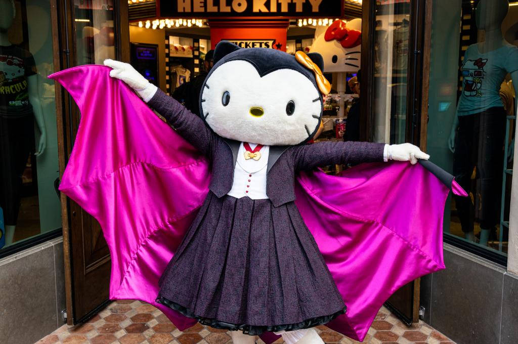 真人大小蝙蝠Hello Kitty萬聖節 壁紙 — Hello Kitty 穿著蝙蝠裝，搭配亮粉色翅膀，自豪地站在主題商店外。