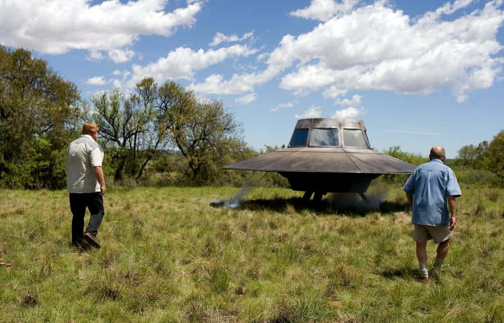 兩個男人在多雲的天空下檢查草地上的大型UFO模型。