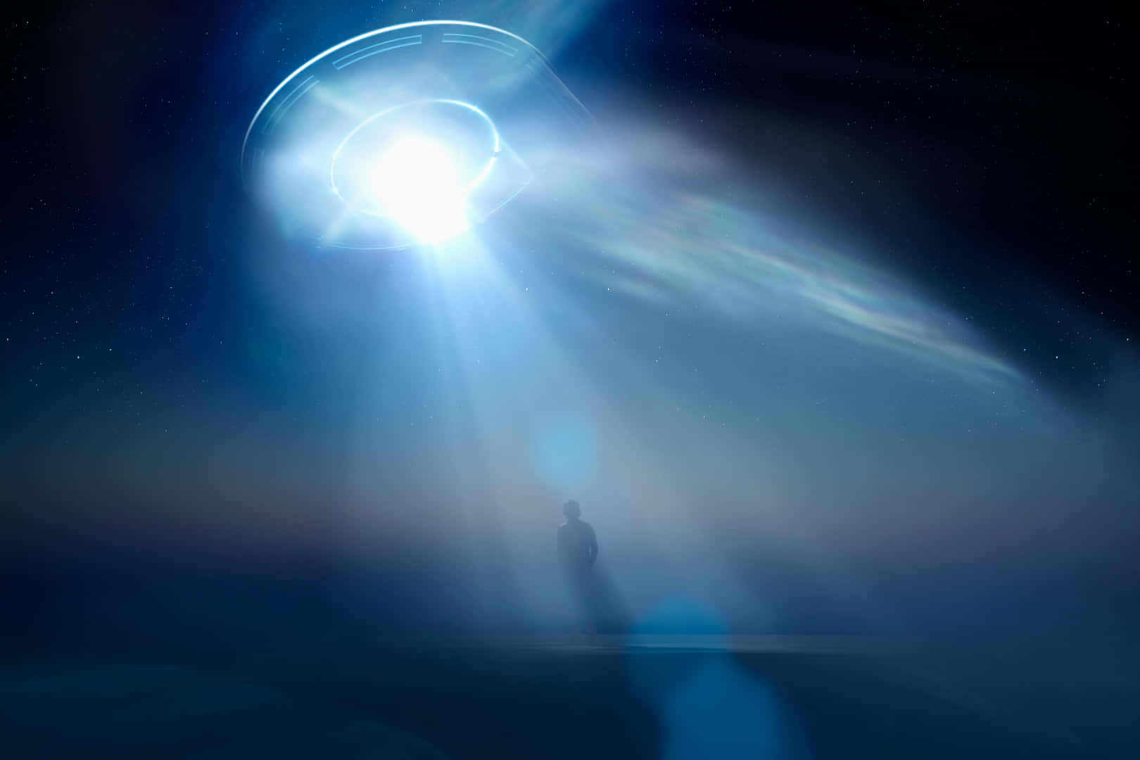 真實UFO藍光效應與人影圖像 壁紙 — 一個孤獨的身影站在發光的UFO下方，UFO在繁星點點的夜空中投射出耀眼的光束。