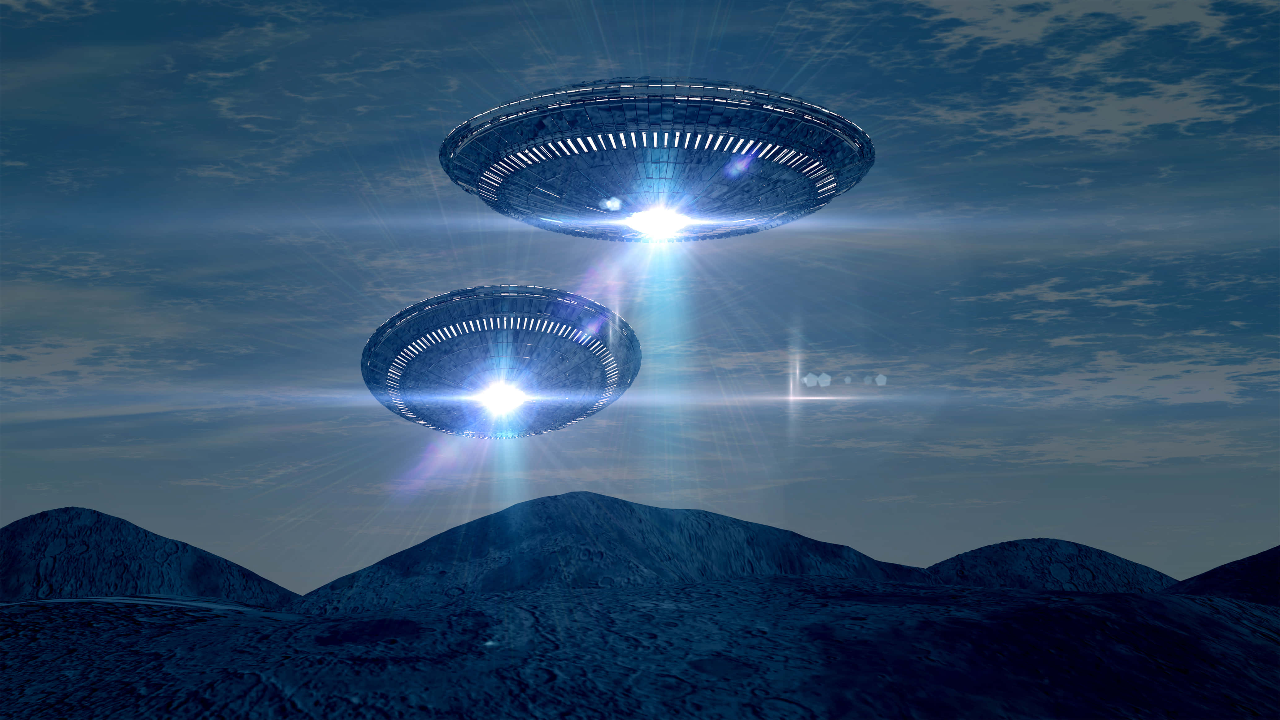 真實UFO飛越山巒光效圖像 壁紙 — 兩個發光的飛碟形UFO在陰雲密布的暮色天空下盤旋在黑暗的山脈之上。