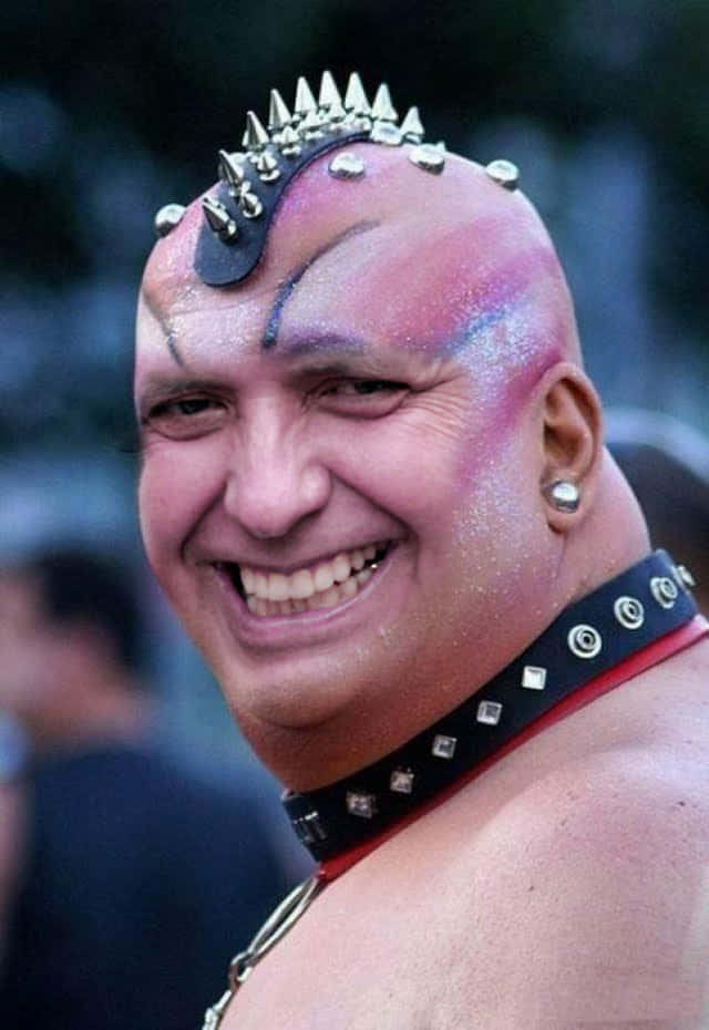 留著尖刺莫霍克頭和閃亮臉部顏料的男人戴著鉚釘項圈微笑。