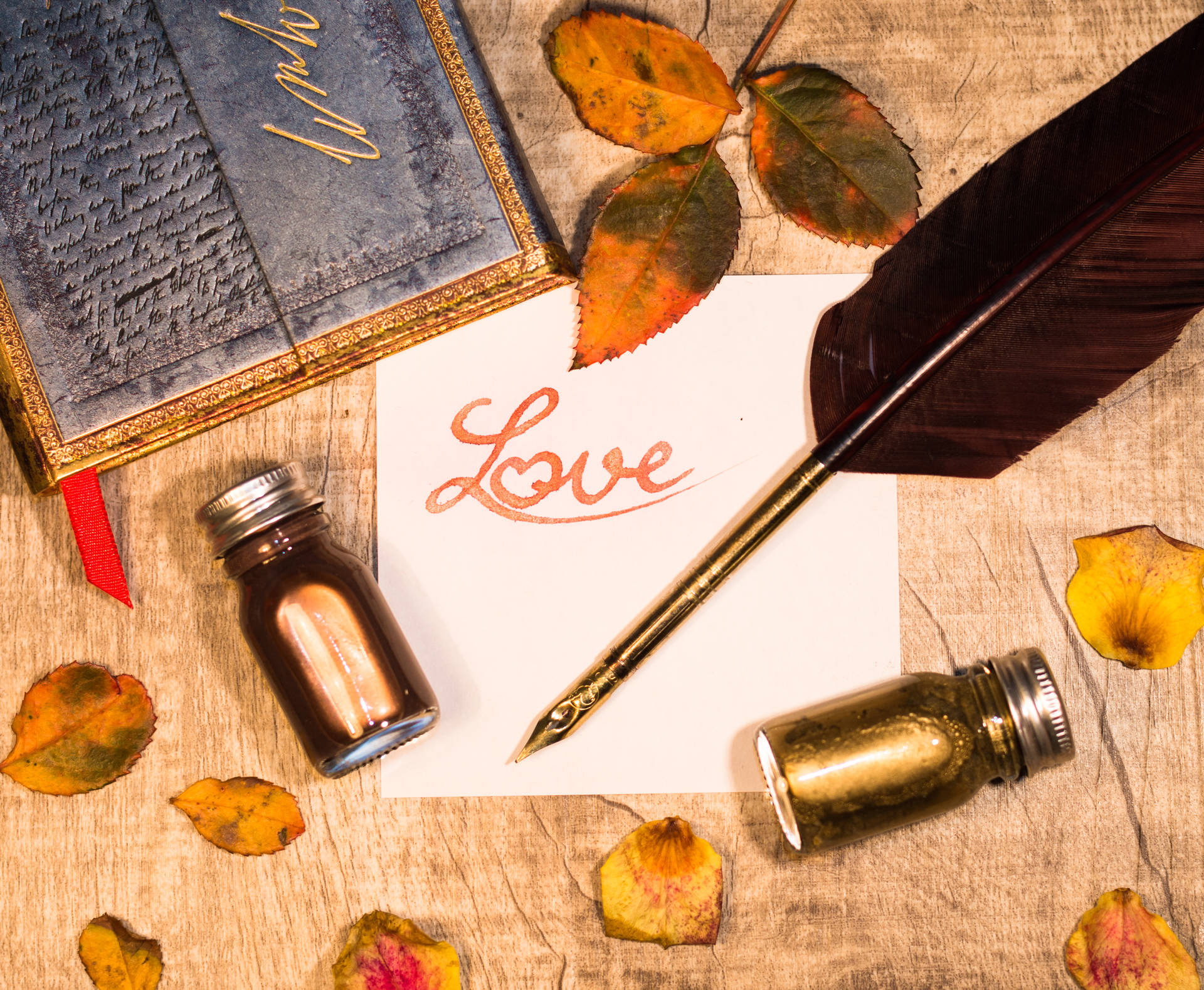 一張手寫便條，上面有「Love」，周圍環繞著秋葉和書寫工具，放在木頭上。