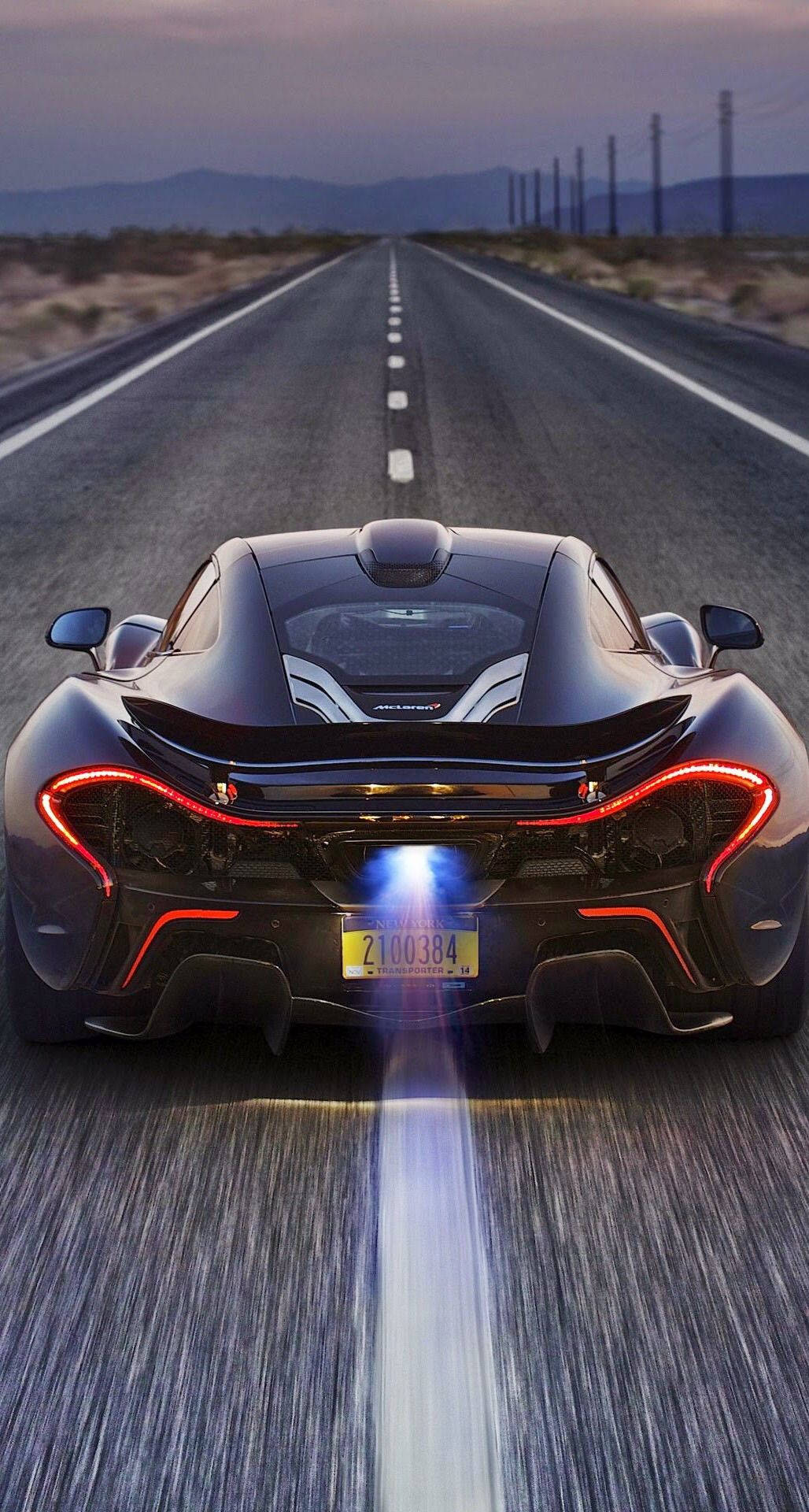 真正酷炫跑車麥拉倫P1後視圖 壁紙 — 一輛黑色McLaren P1在黃昏時分於沙漠公路上疾馳，帶有發光的紅色尾燈和藍色排氣火焰。