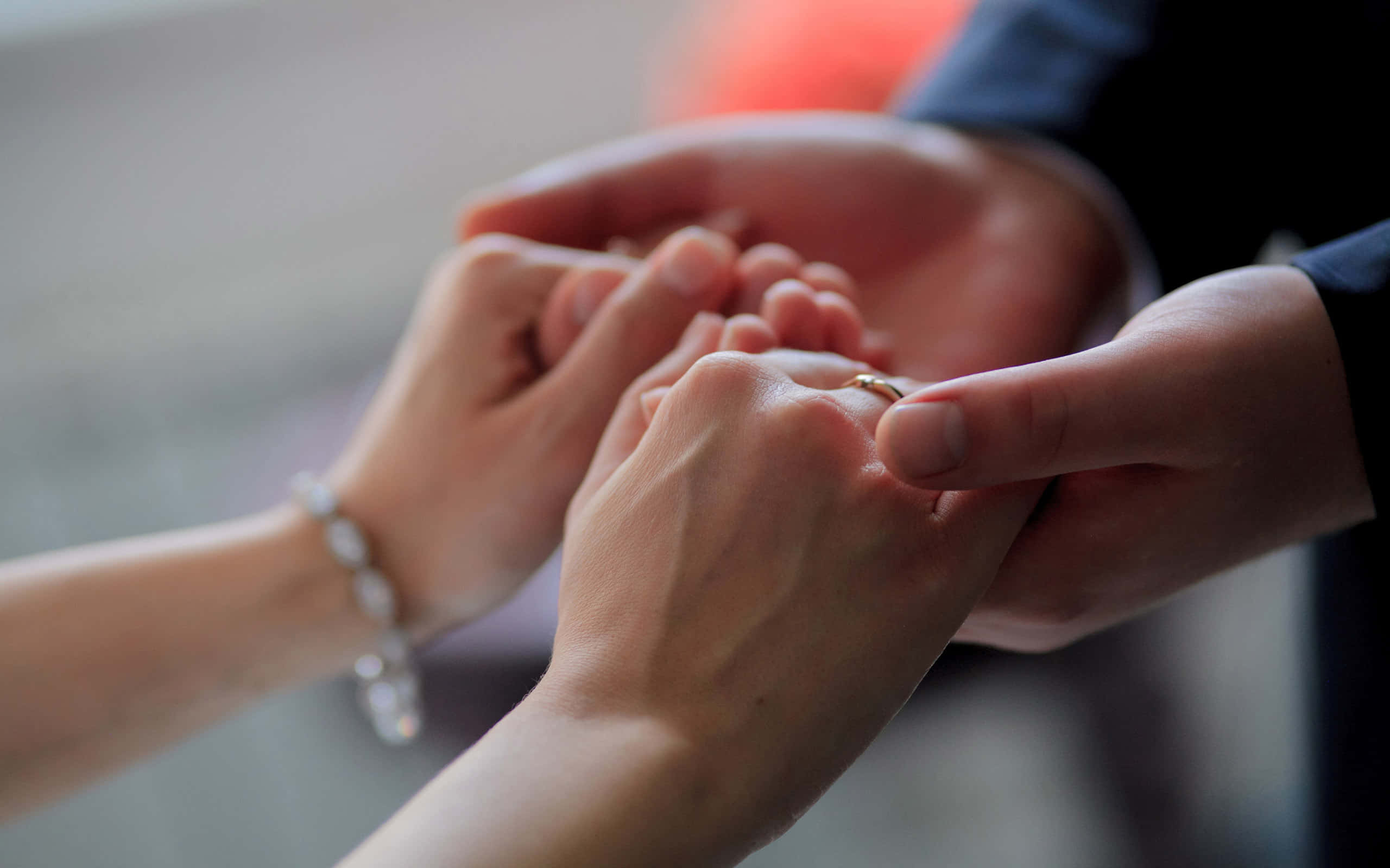真誠情侶牽手照片 壁紙 — 一張特寫照片，雙手輕輕地將金色結婚戒指戴在手指上，背景柔和模糊。