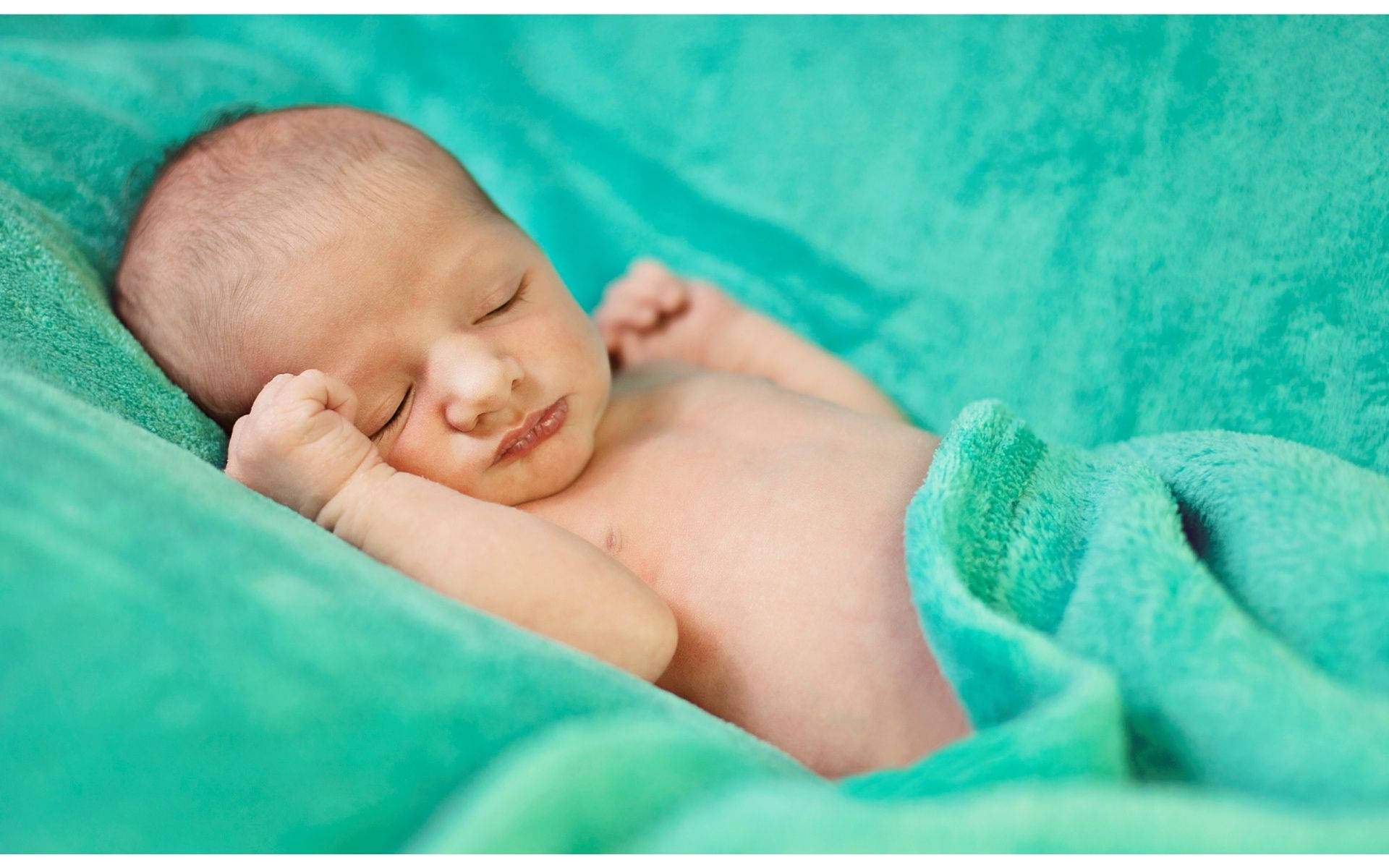睡在柔粉綠毯上的嬰兒 壁紙 — 一個平靜的新生嬰兒在柔軟的青色毯子上安睡，小拳頭蜷曲在臉旁。