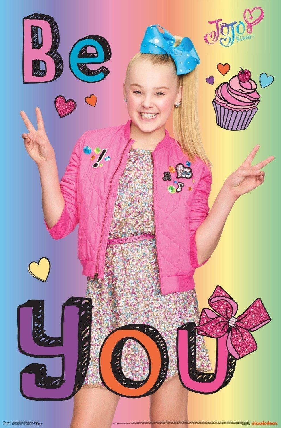 Jojo Siwa 在彩虹背景中比出和平手勢微笑，背景有心形和杯子蛋糕。