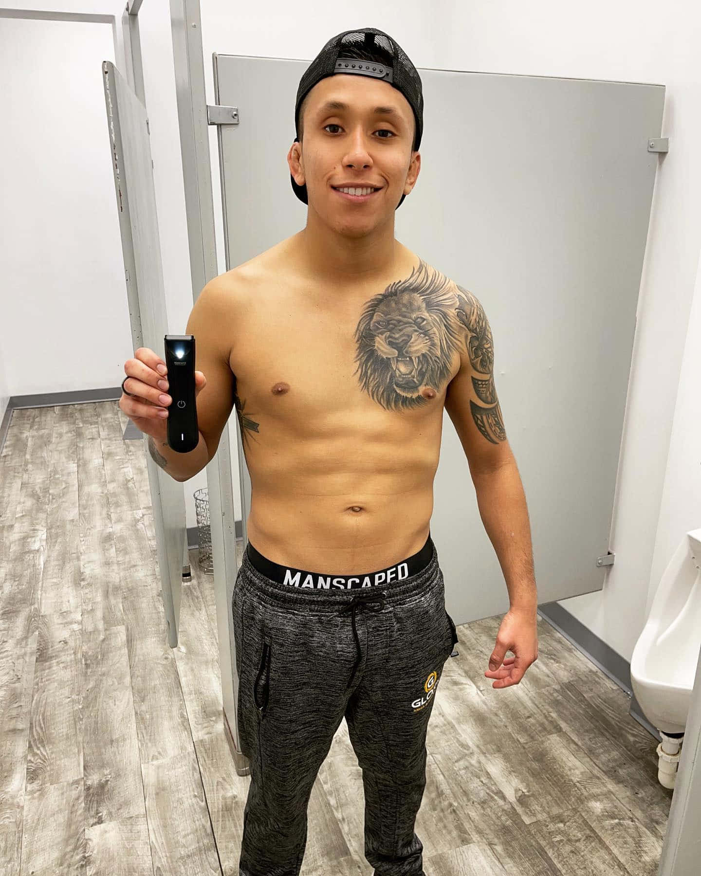 一位肌肉發達的男子，有獅子紋身，微笑著在浴室中拿著修剪器。