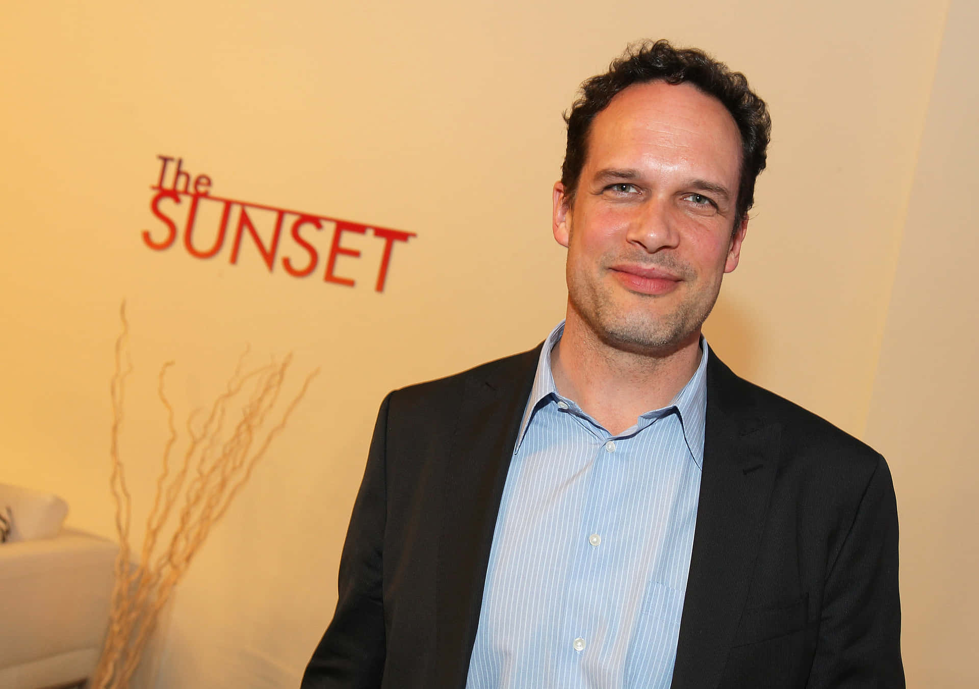 身穿西裝的男子在活動中微笑，身後有「The SUNSET」標誌。