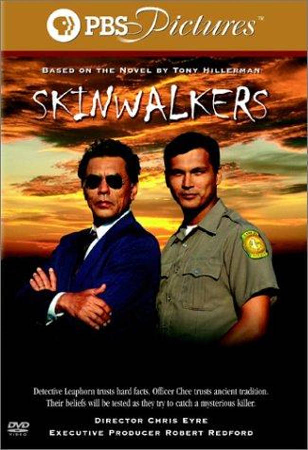 知名演員亞當·比奇出演《Skinwalkers》 壁紙 — 兩個男人自信地站在火熱的日落天空前，一個穿西裝戴太陽眼鏡，另一個穿制服，上方有PBS Pictures標誌。