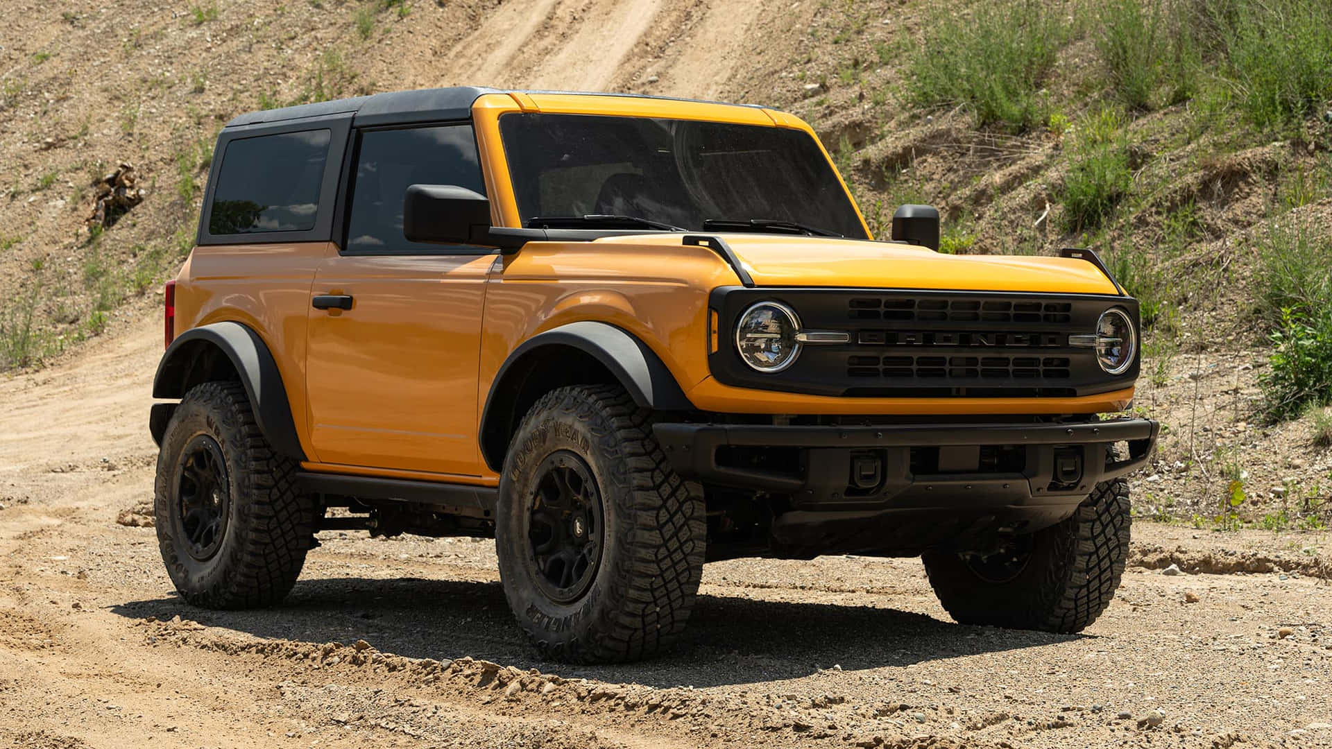 橙色福特Bronco SUV停放在草坡上的泥路上。