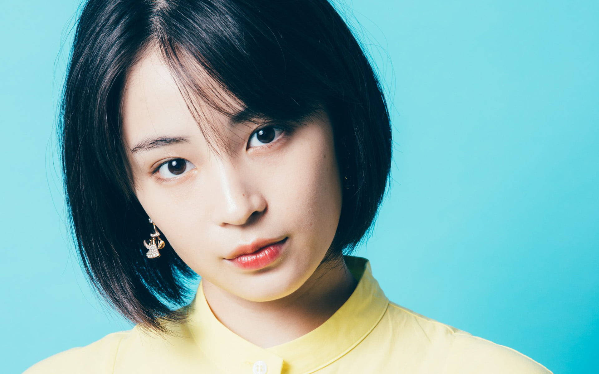 短黑髮、身穿黃色襯衫的年輕女性，藍色背景
