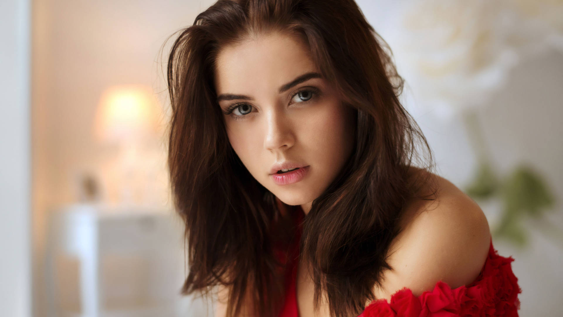 短髮美麗女性 壁紙 — 一位棕色頭髮、綠色眼睛的年輕女性，穿著紅色露肩上衣，在柔和光線的室內環境中直視鏡頭。