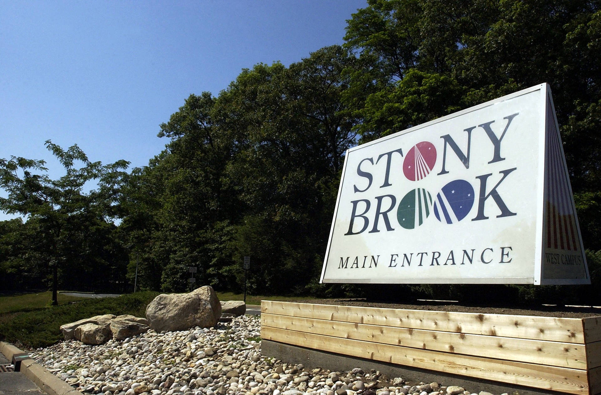 Stony Brook 主入口標牌，周圍環繞著樹木和碎石，在晴朗的藍天下。
