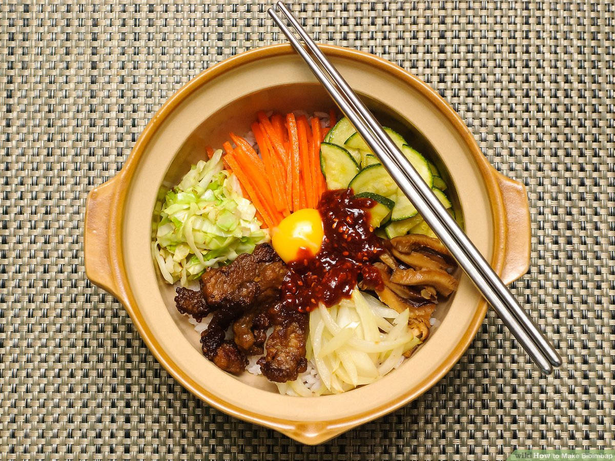 石鍋熱騰騰的拌飯 壁紙 — 俯瞰一碗冒煙的韓國石鍋拌飯，上面有色彩繽紛的蔬菜、肉類和生蛋黃，並以筷子點綴。
