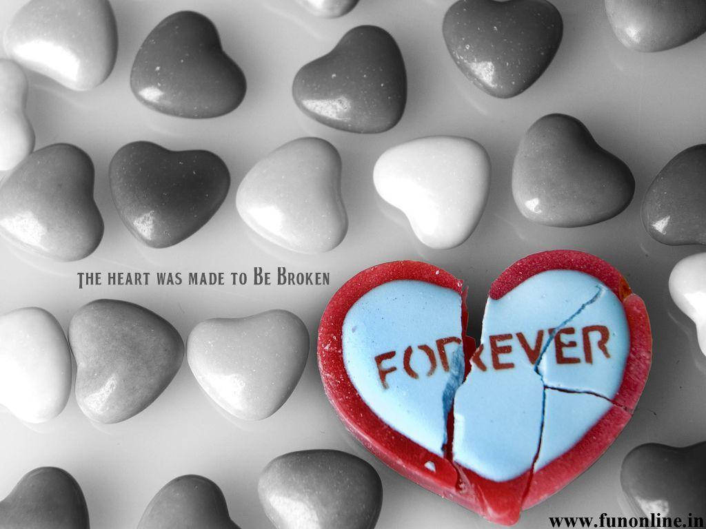 一顆破碎的心形糖果，上面寫著「FOREVER」，放在灰色心形石頭之間。
