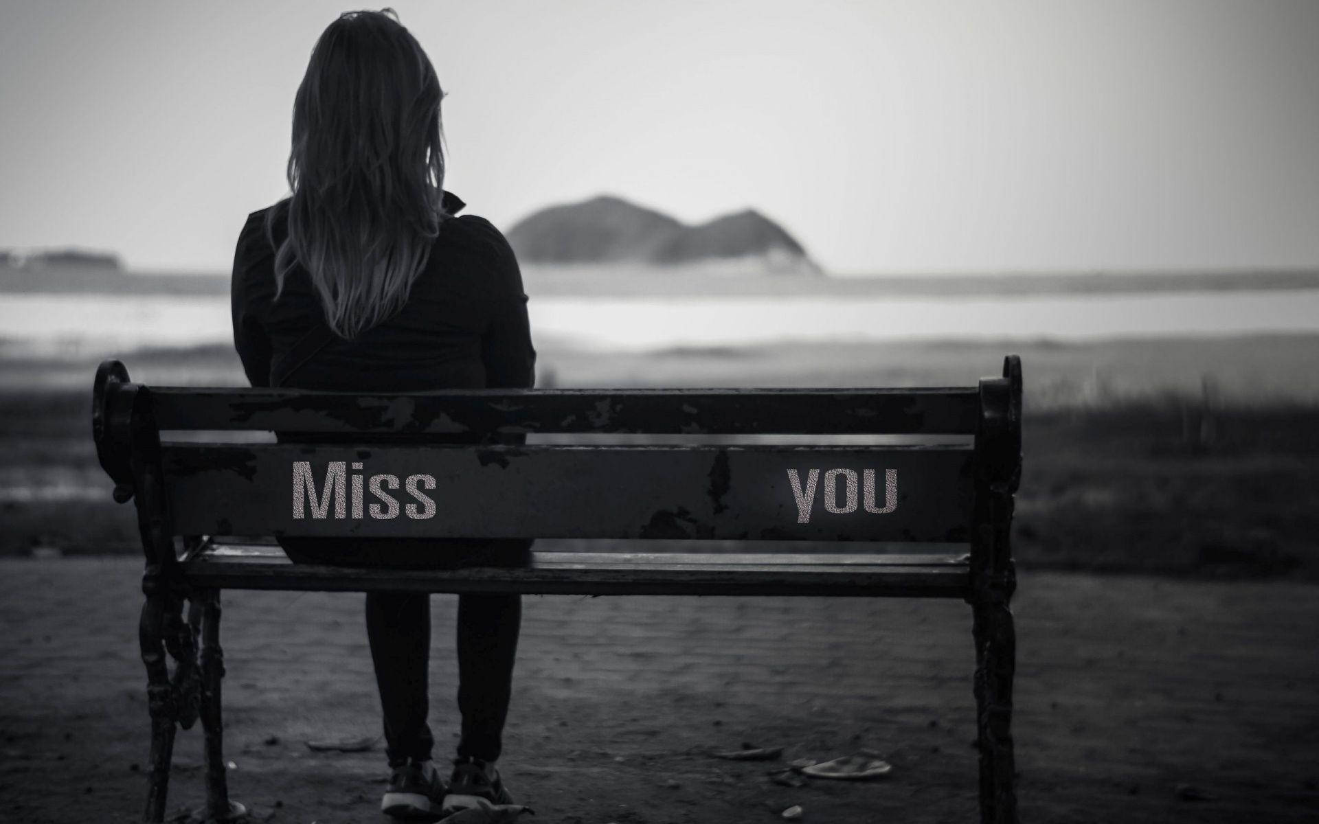 一個人獨自坐在海邊的長椅上，上面寫著「Miss you」。