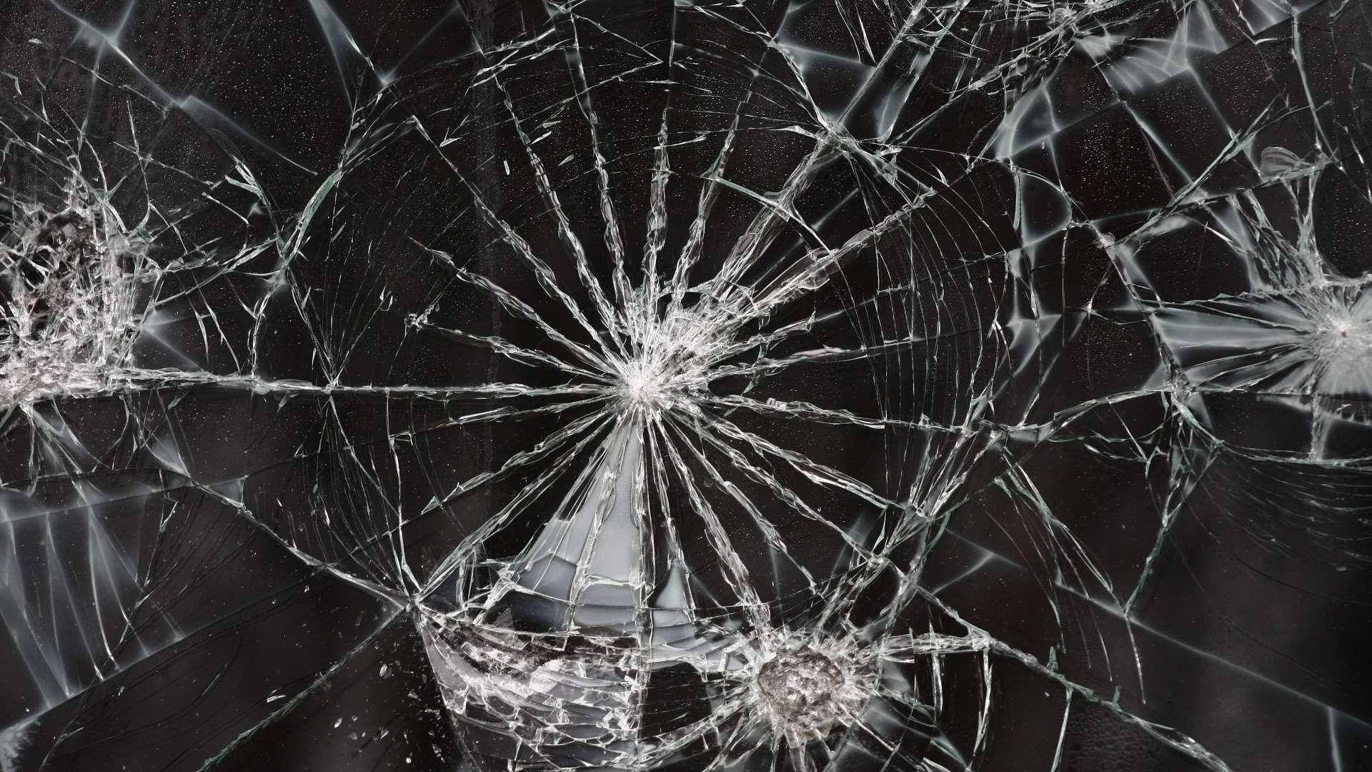 裂屏 桌布 壁紙 — 破碎的玻璃表面，在深色背景下，撞擊點散發出複雜的裂紋。