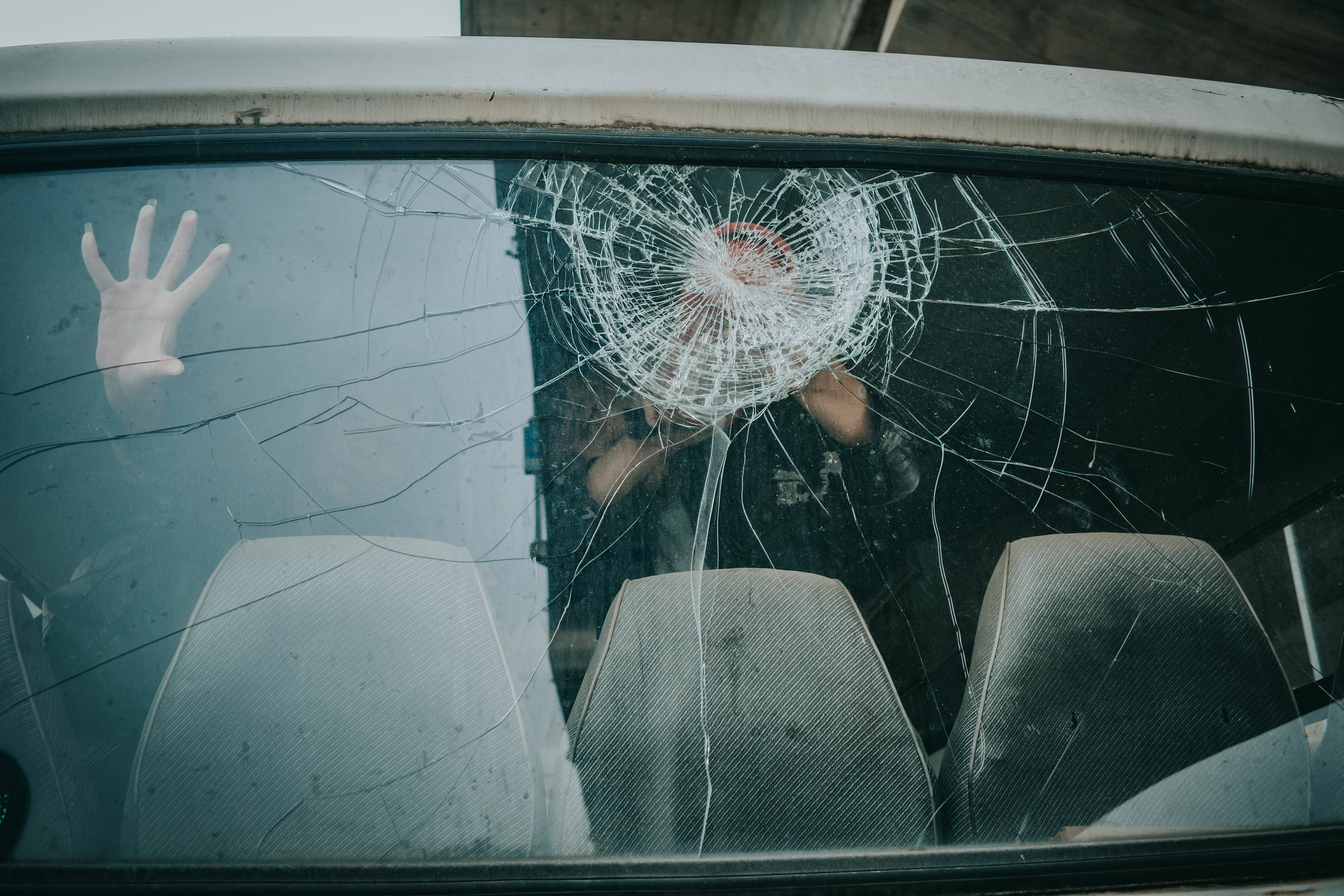破碎車尾擋風玻璃 壁紙 — 一個人的手按壓在一個帶有蜘蛛網狀裂紋圖案的破碎車窗上。