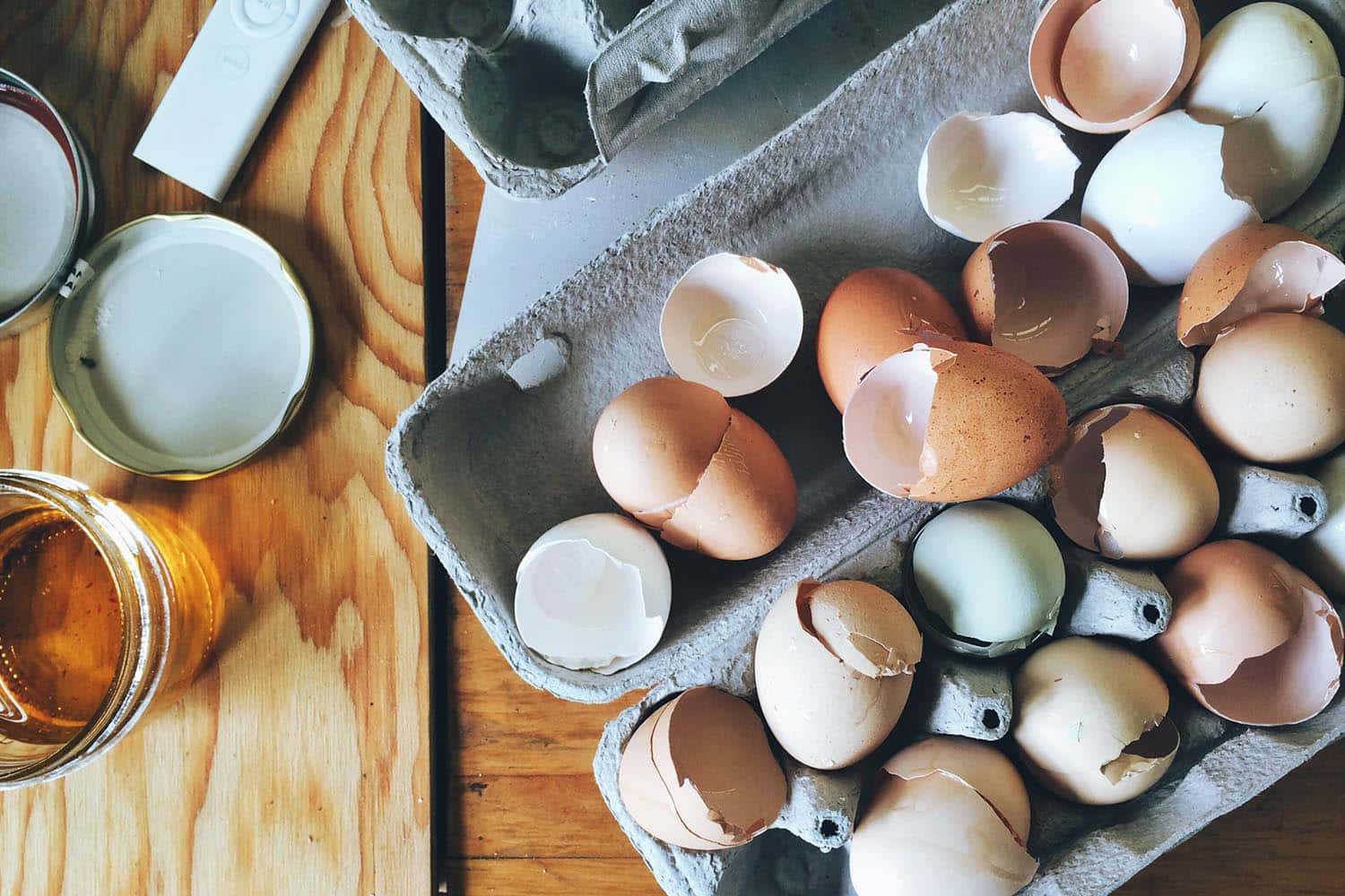 Eggshell 桌布 壁紙 — 破裂的蛋殼和完整的雞蛋從一個紙板盒中溢出，放在溫暖的木桌上，旁邊有一罐蜂蜜。