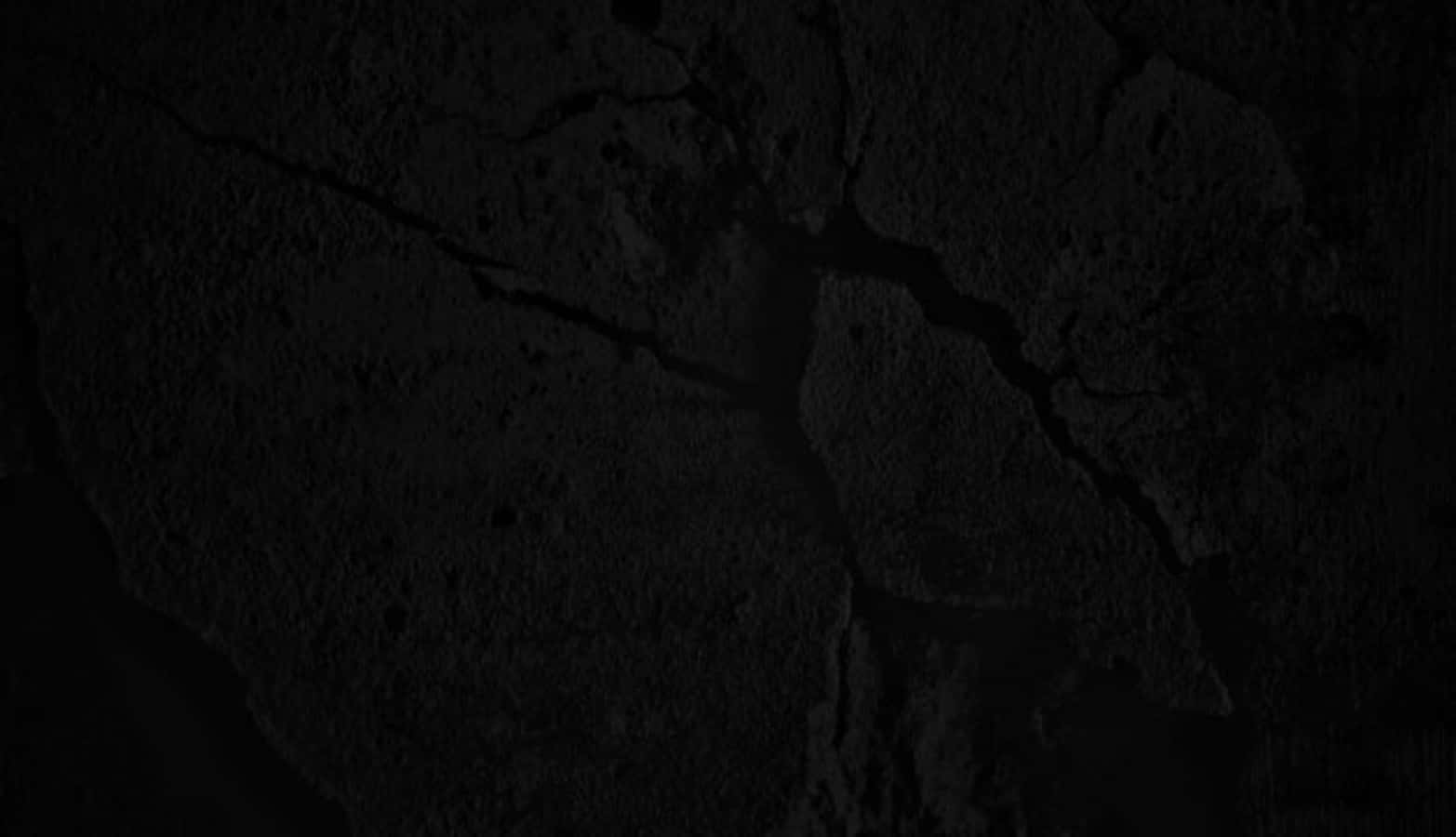 碎混凝土黑色紋理圖案 壁紙 — 微光下粗糙紋理及深裂縫的黑色裂面特寫。