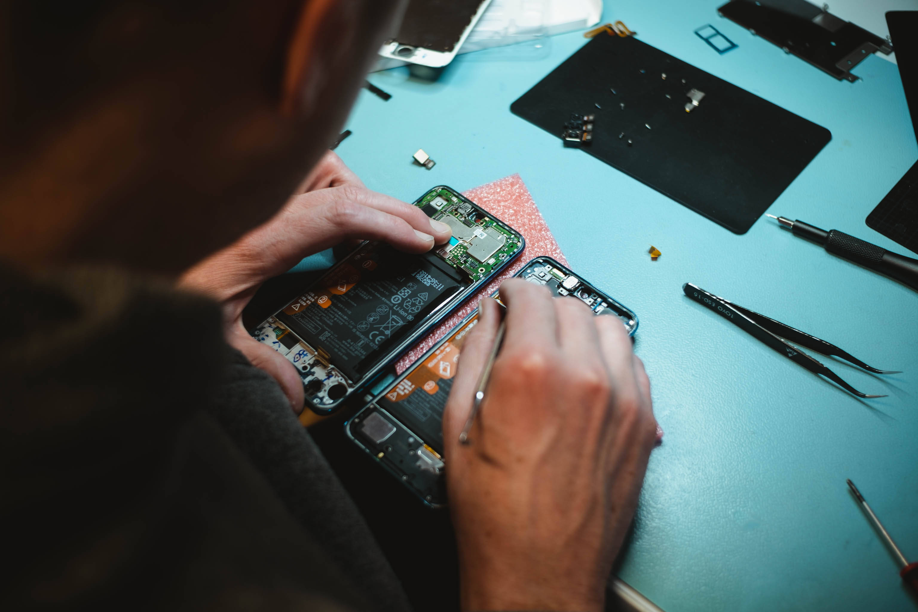 碎裂手機維修 壁紙 — 從上方俯瞰技術人員在藍色工作台上用工具仔細維修智能手機電路板。