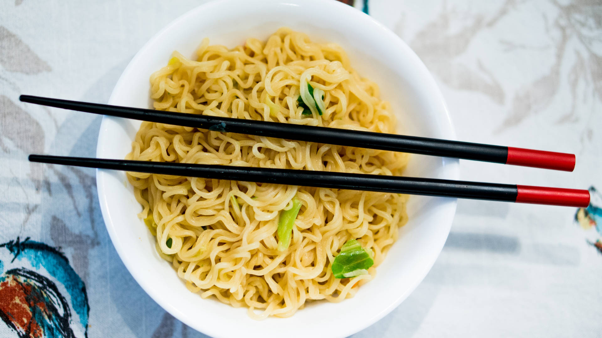 一碗即食麵配筷子，放在有圖案的桌布上。