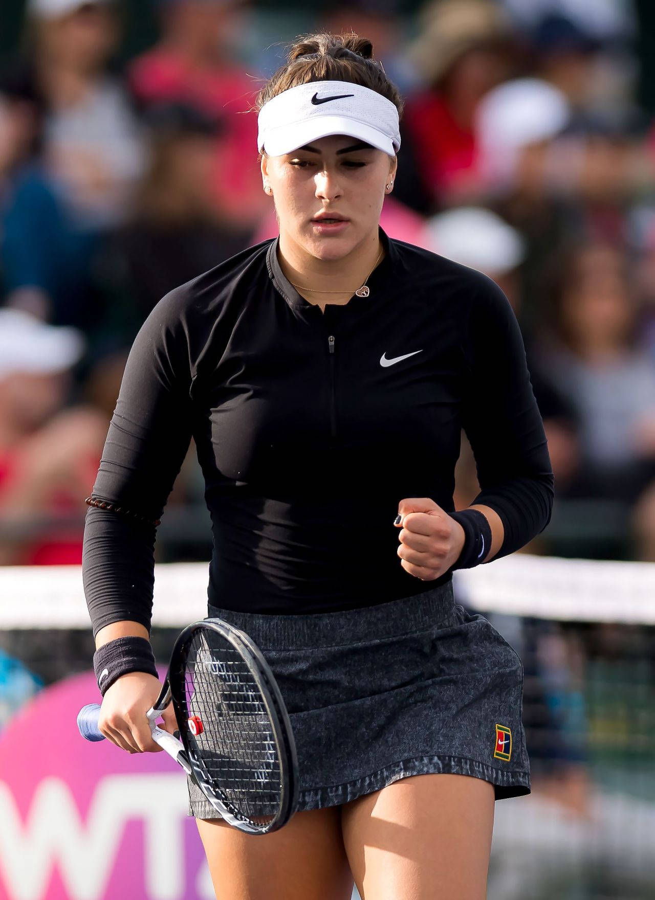 女網球運動員穿著黑色Nike服裝，在陽光明媚的球場上比賽時握著球拍。