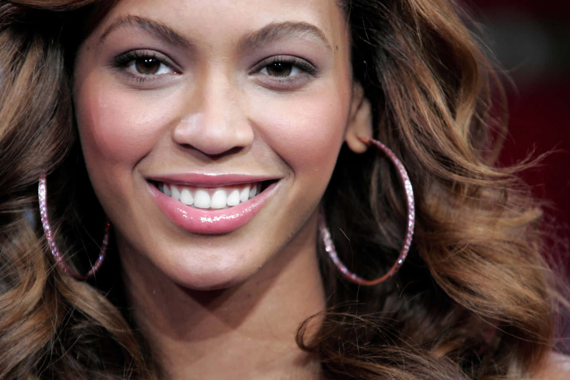 Beyoncé 微笑，戴著大圈形耳環，波浪棕色頭髮。