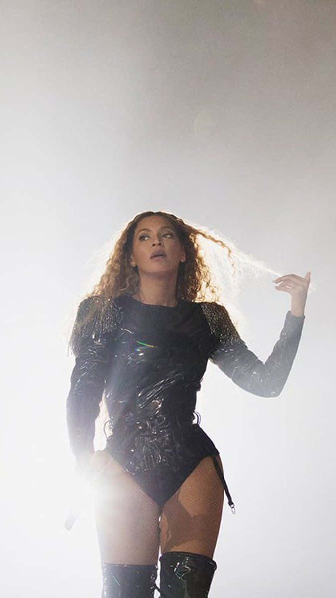 碧昂絲展現閃耀金屬風采 壁紙 — Beyonce 身穿閃亮黑色連體衣，在明亮的舞台燈光下表演，秀髮飄逸。