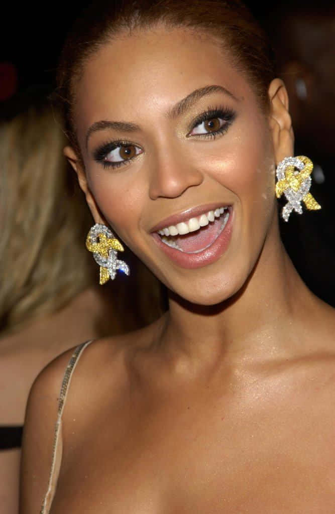 Beyoncé 在正式聚會中戴著閃閃發光的蝴蝶結耳環咧嘴笑。