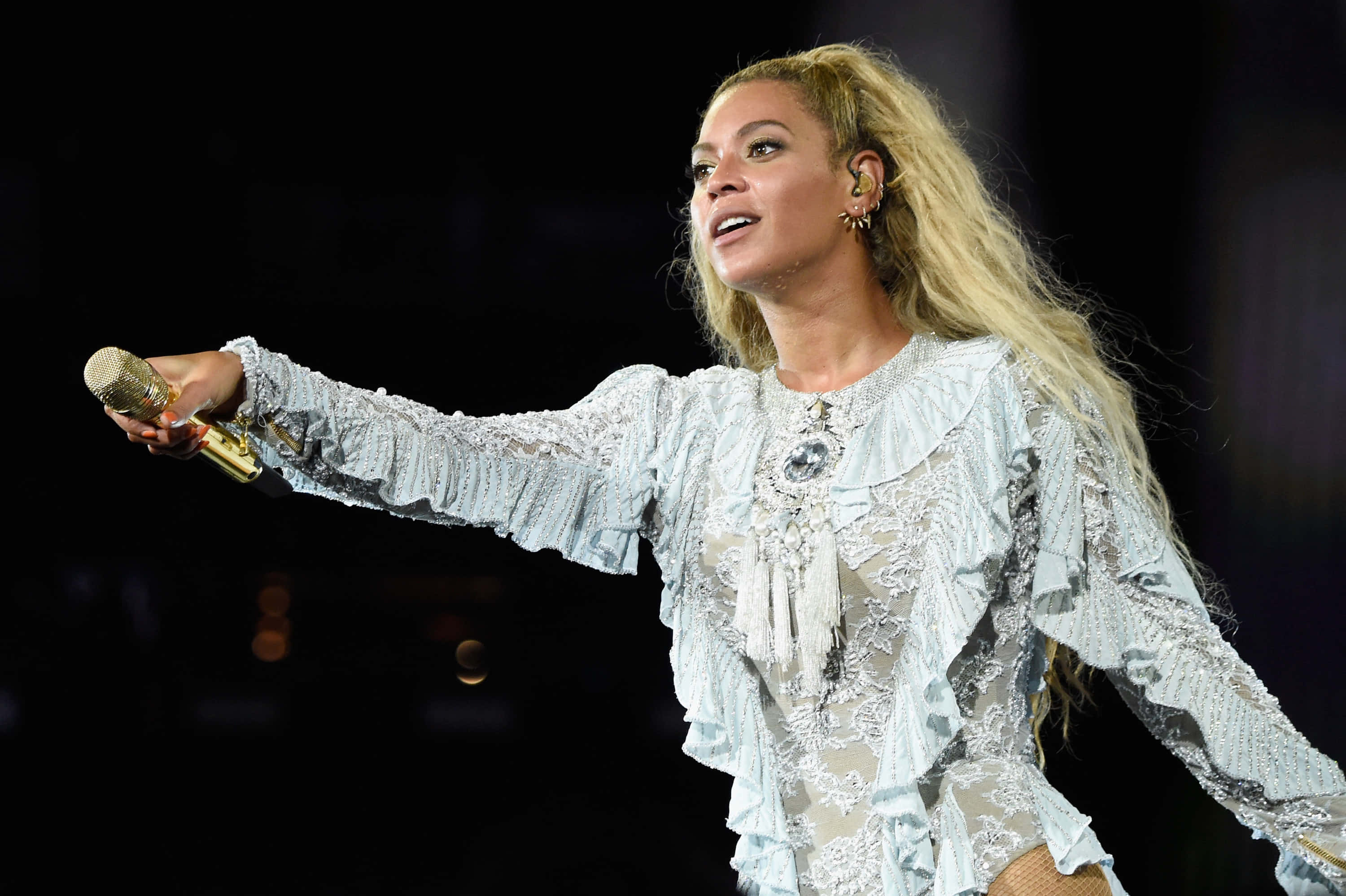 碧昂絲氣質高貴風采卓絕 壁紙 — Beyoncé 在舞台上穿著精緻的淺藍色蕾絲服裝，手持金色麥克風，在舞台燈光下表演。
