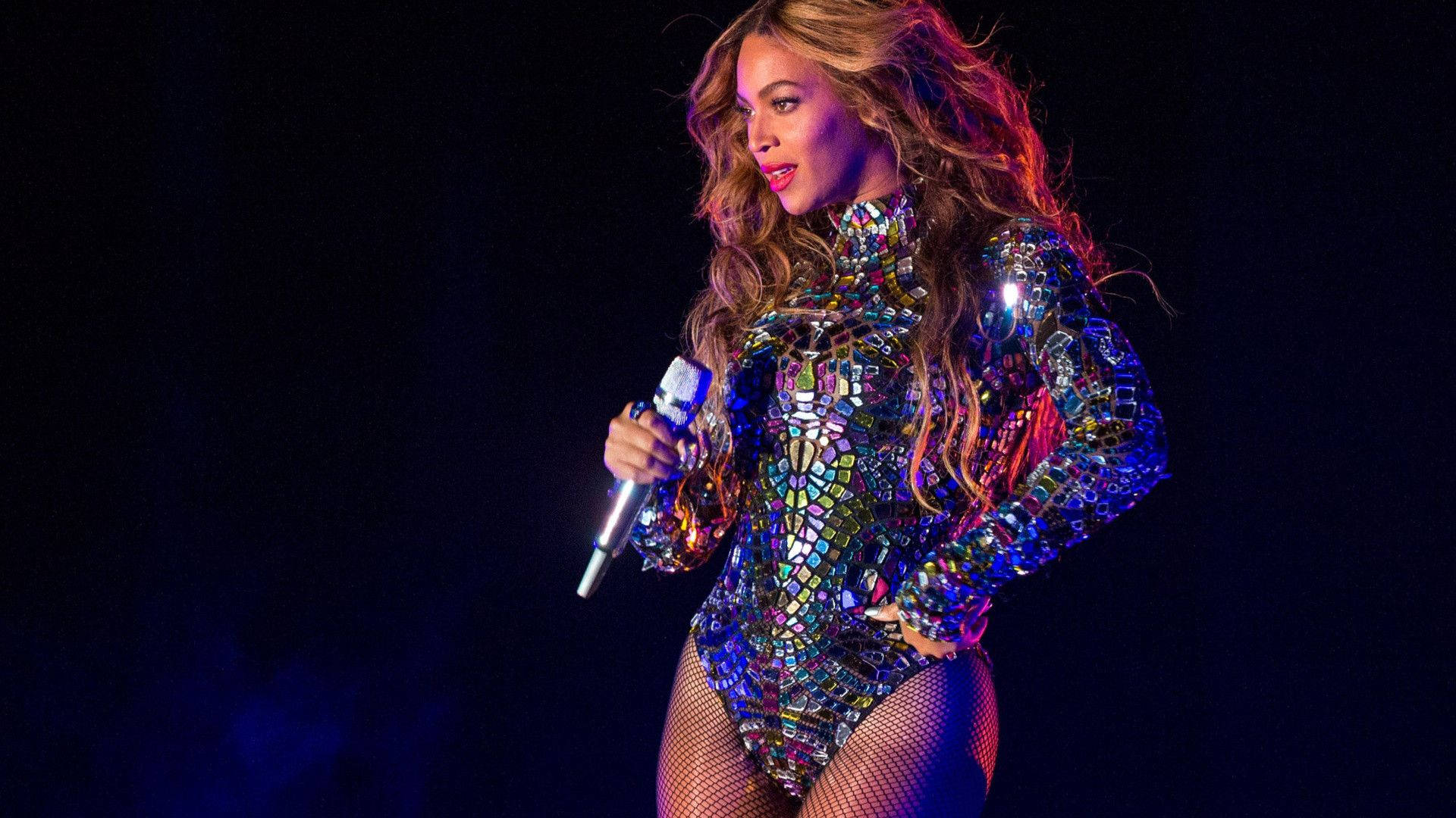 Beyonce 在舞台上穿著閃閃發光的緊身衣，手持麥克風唱歌