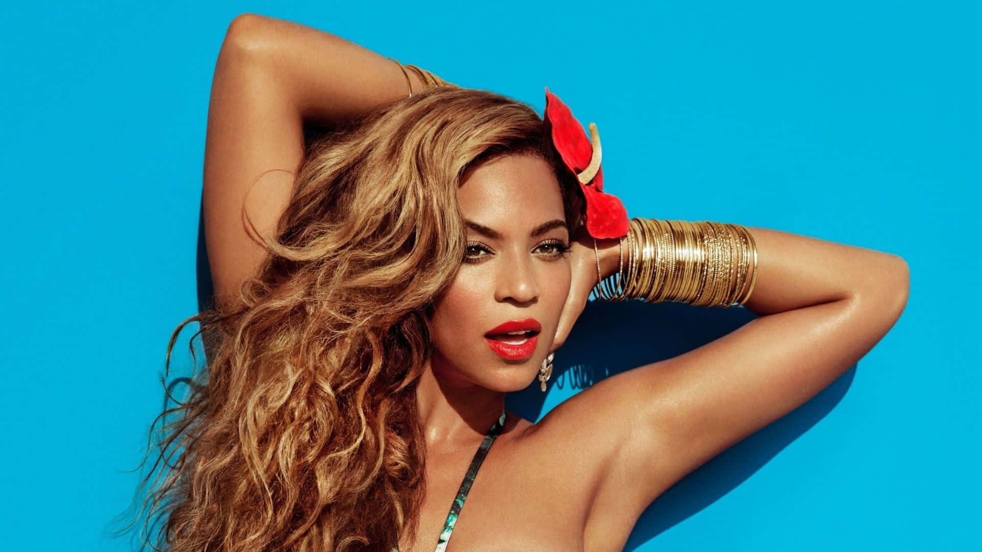 碧昂絲身穿標誌性黃色裹身裙展現強悍氣勢 壁紙 — Beyonce 在充滿活力的藍色背景前自信地擺姿勢，長長的波浪形頭髮和鮮豔的紅色唇膏。