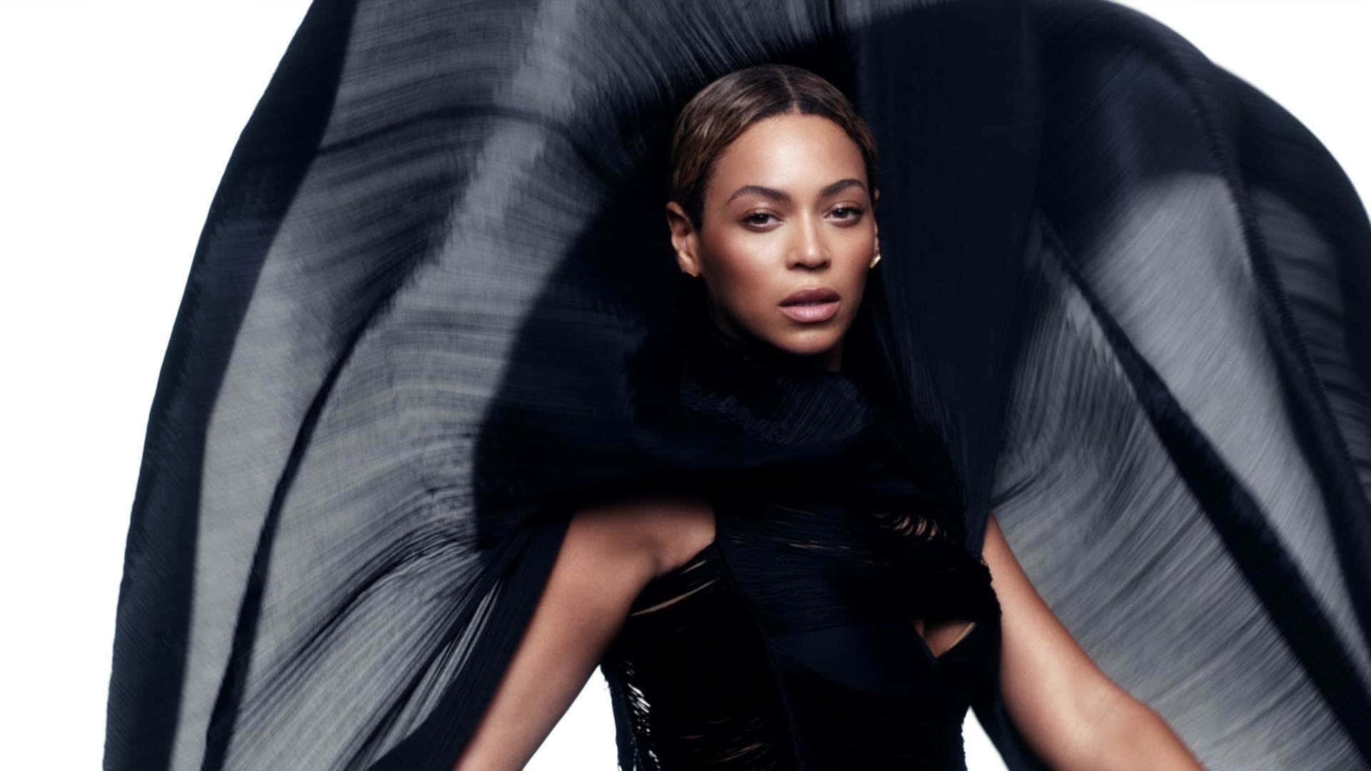 碧昂絲身著淺藍色禮服閃耀光芒 壁紙 — Beyoncé 強烈凝視，被戲劇性飄逸的黑色布料框住，背景是純白色。