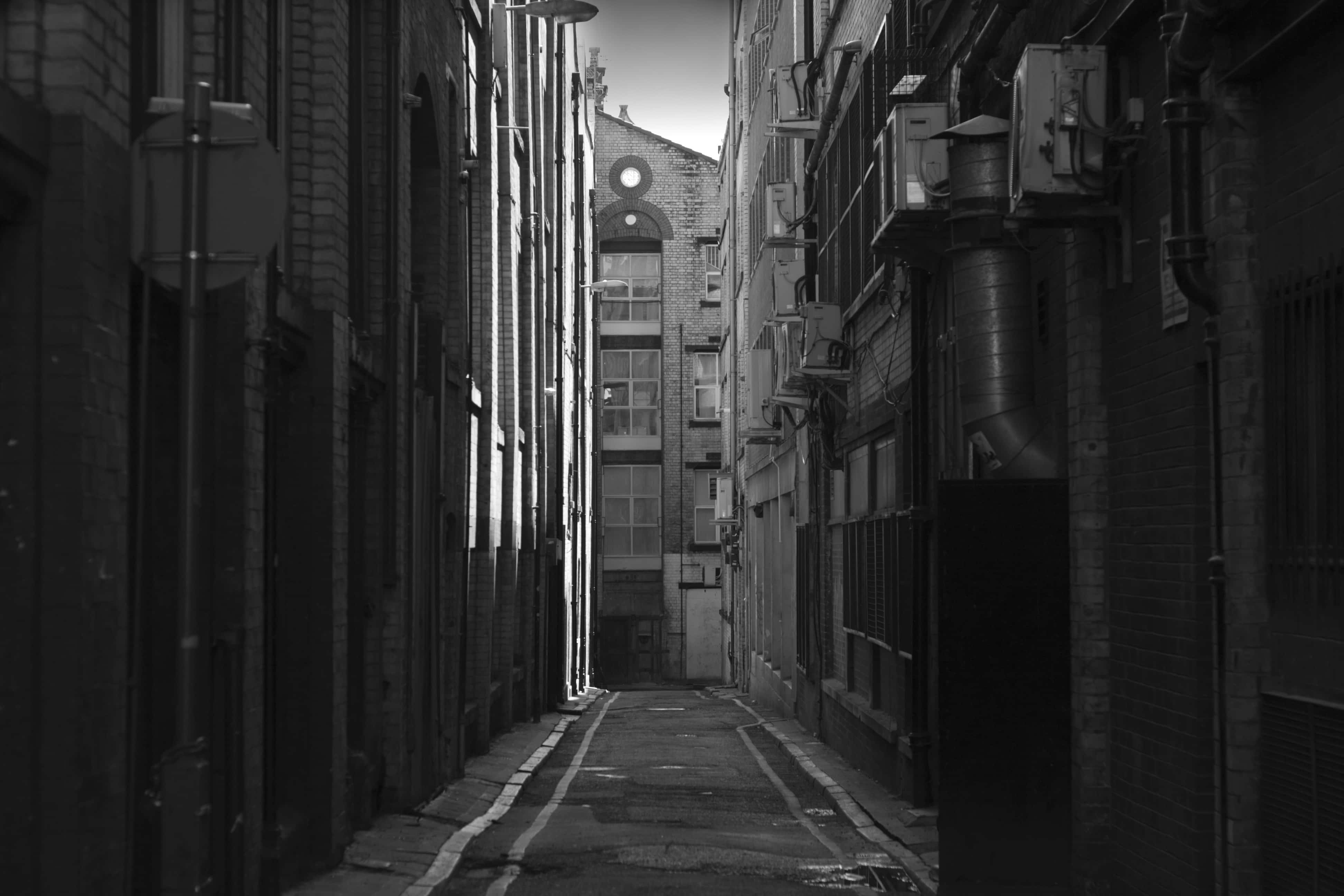 Alleyway 桌布 壁紙 — 磚建築物之間一條狹窄的黑白小巷，通向明亮天空下遠處的拱形窗戶。