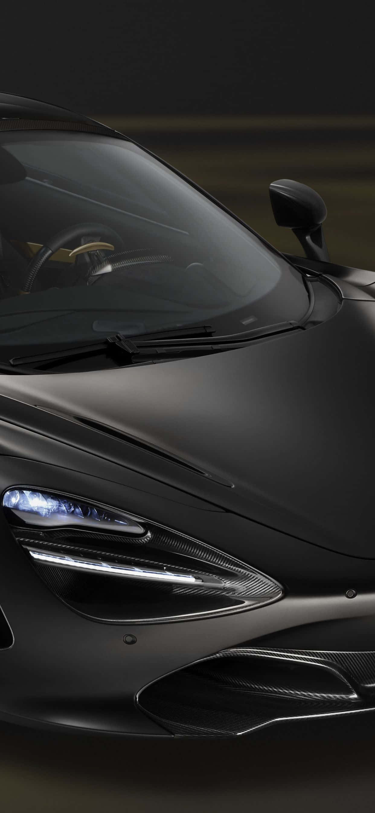 磨砂黑 iPhone Xs Max McLaren 720s 背景 壁紙 — 一輛時尚的啞光黑色跑車，在昏暗的環境中帶有發光的車頭燈和碳纖維飾件。