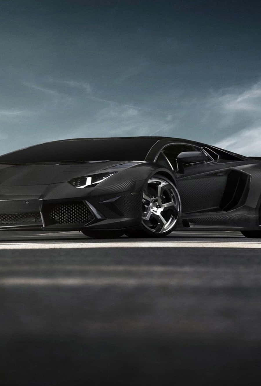 啞光黑色林寶堅尼 Aventador 配碳纖維飾邊，停在黑暗道路上，天空灰色。