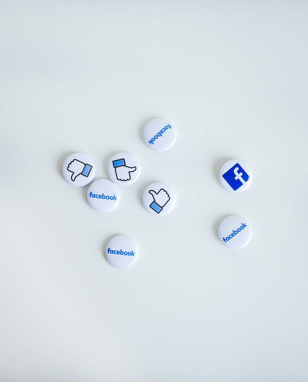 社交媒體 Facebook 圖標 壁紙 — 白色圓形Facebook品牌按鈕，帶有豎起大拇指和放下大拇指圖標，散落在純淺灰色表面上。