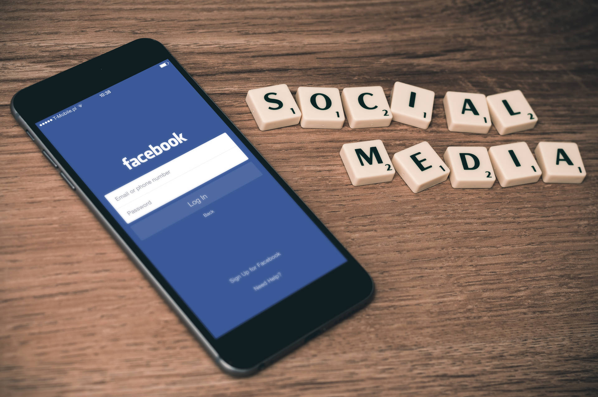 智能手機顯示Facebook登入，旁邊是拼出社交媒體的Scrabble字母磚在木上。