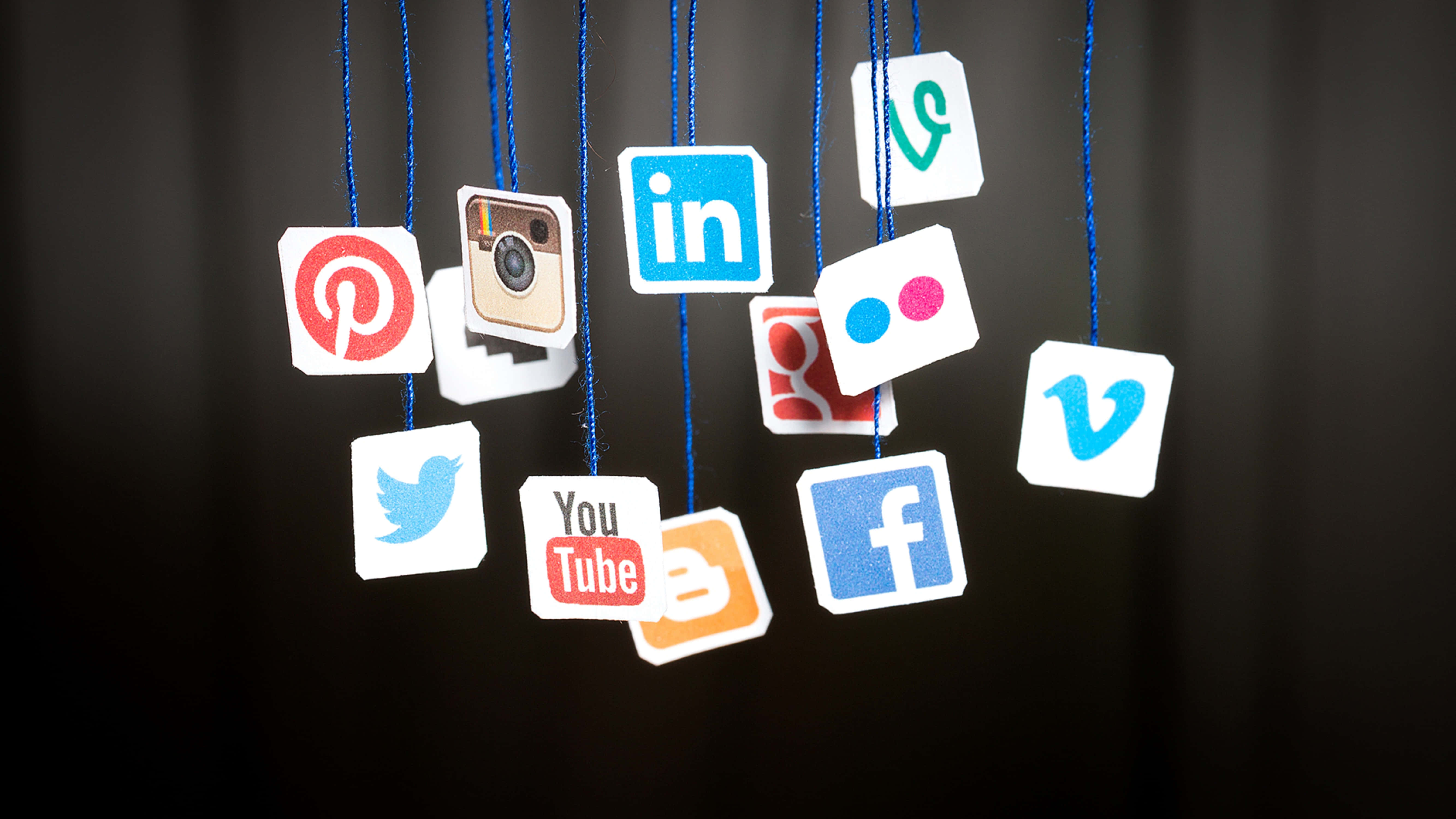 4K Social Media 桌布 壁紙 — 社交媒體標誌像裝飾品一樣掛在藍色繩子上，背景是深色窗簾。