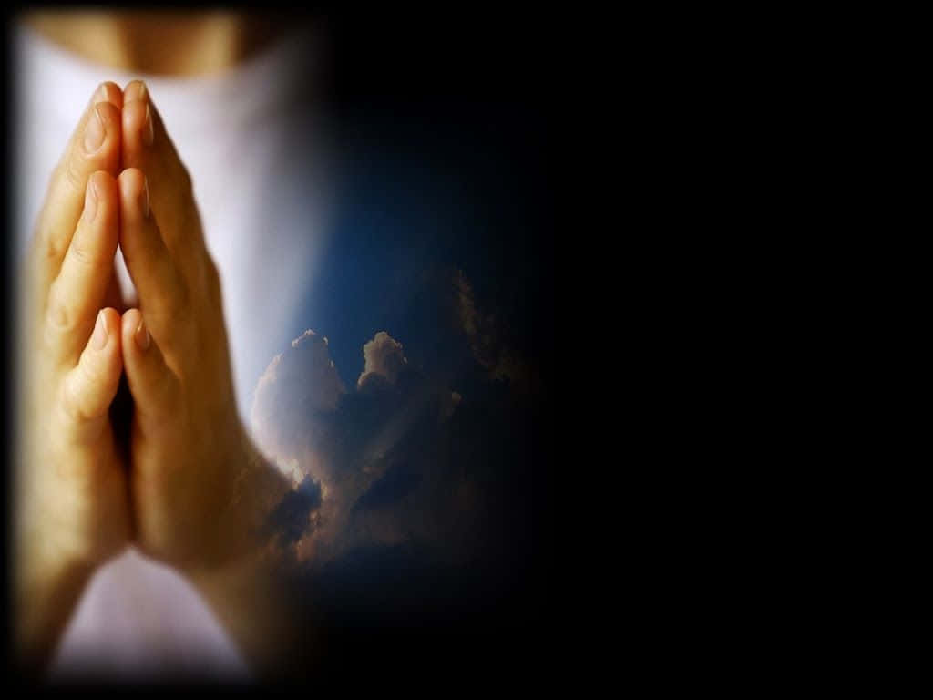 祈禱雙手對比深色背景圖 壁紙 — 雙手合十祈禱的特寫，背景是黑暗且帶有柔和發光的雲層。