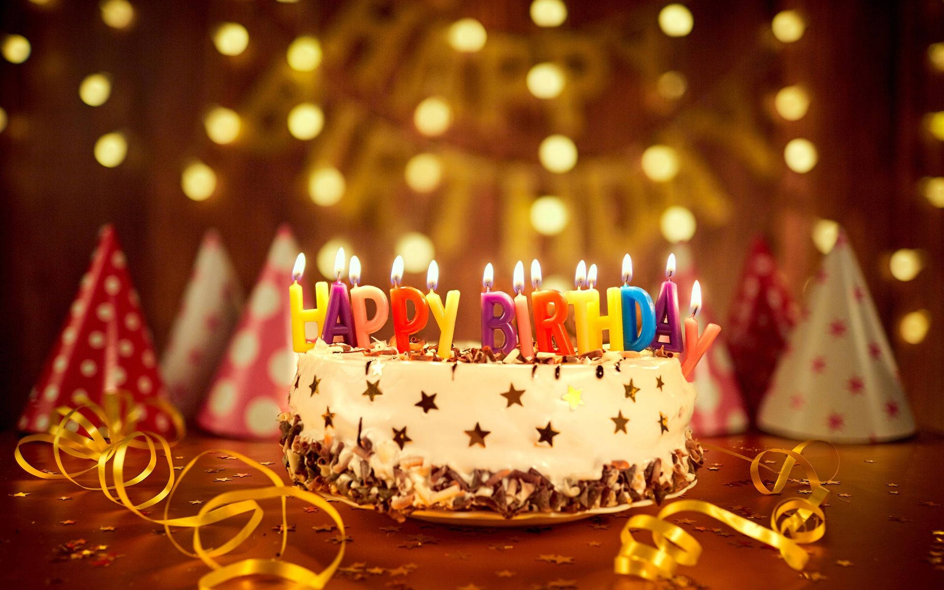 生日蛋糕，上面有燃燒的蠟燭和派對帽，放在節日餐桌上。 — 生日快樂 壁紙