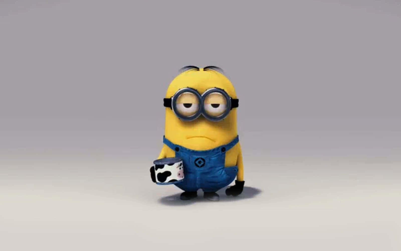 一個黃色卡通Minion在灰色地板上拿著一個牛紋馬克杯。